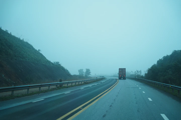 A truck drives on a foggy highway through hills.