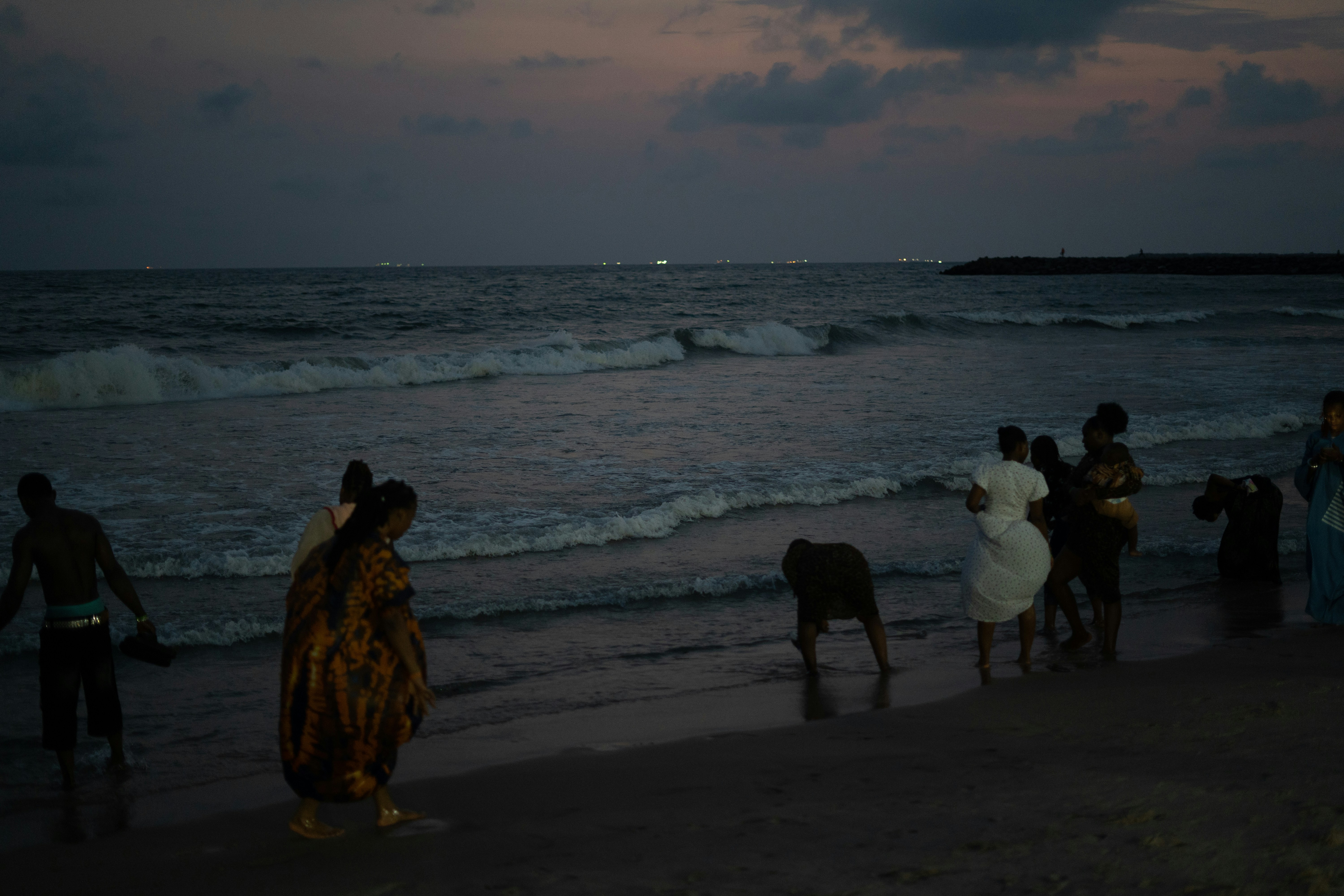 People and a goat on a beach at dusk.