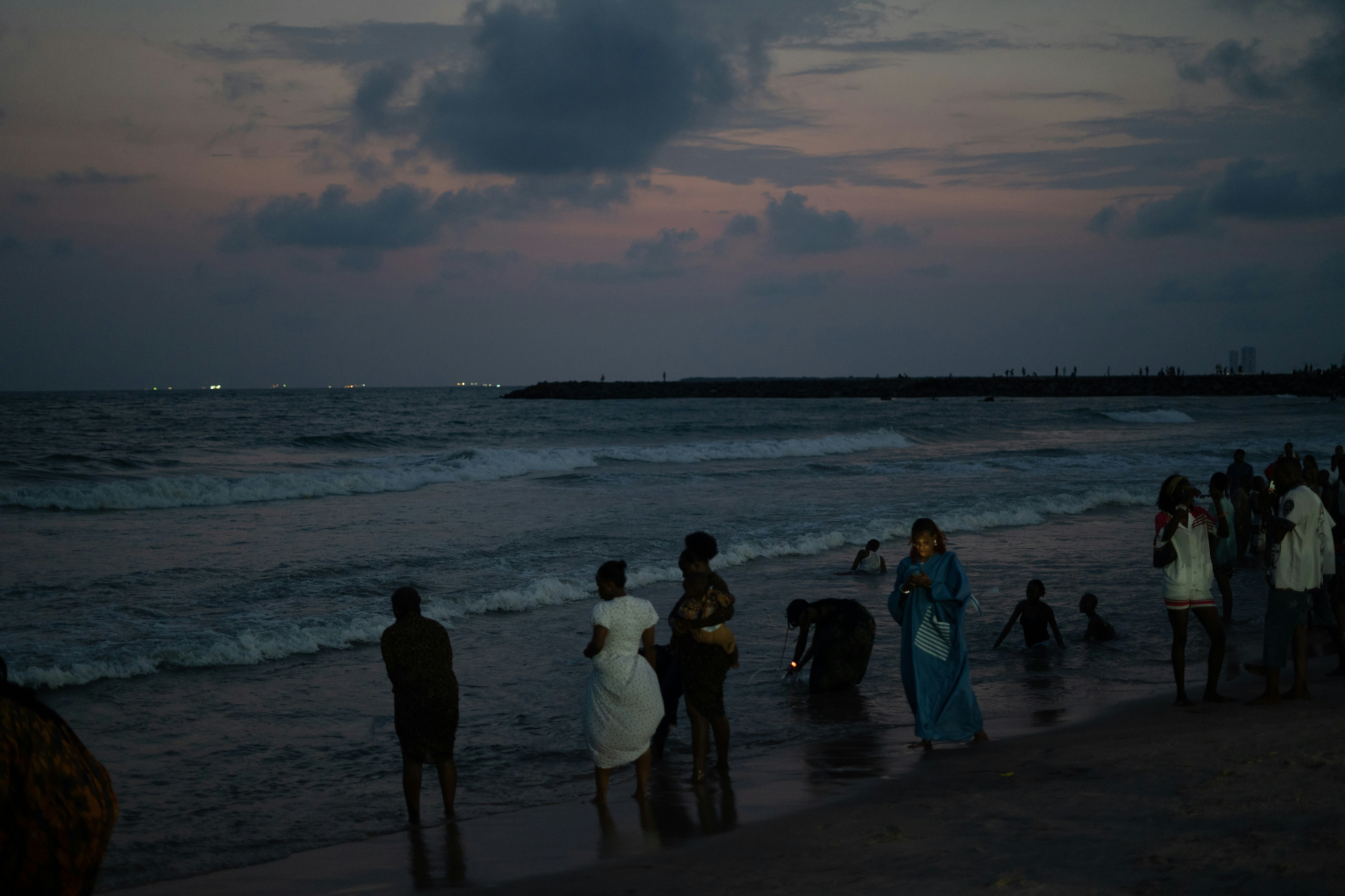 People on a beach at dusk with waves crashing.