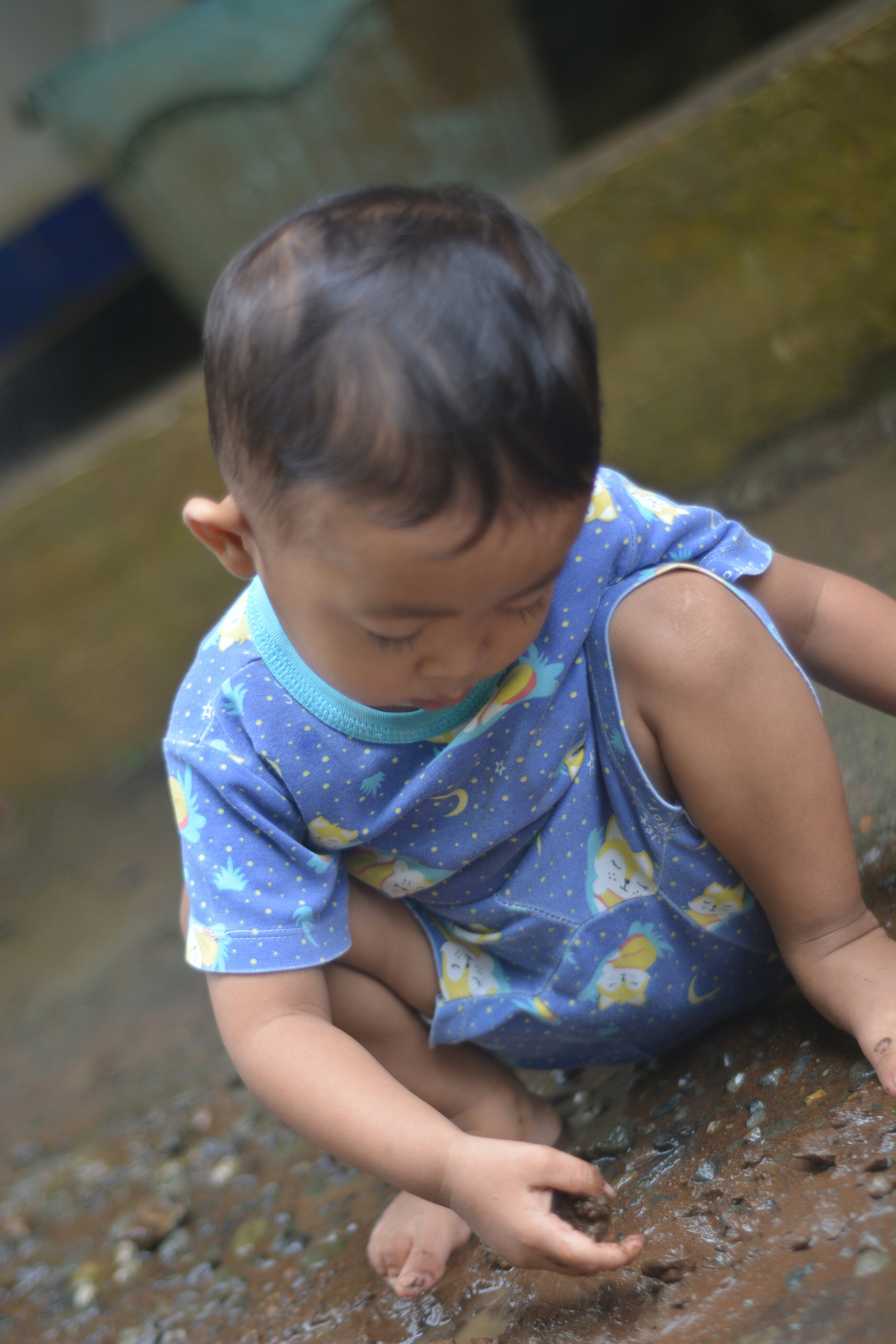 A young child in a blue shirt playing with rocks