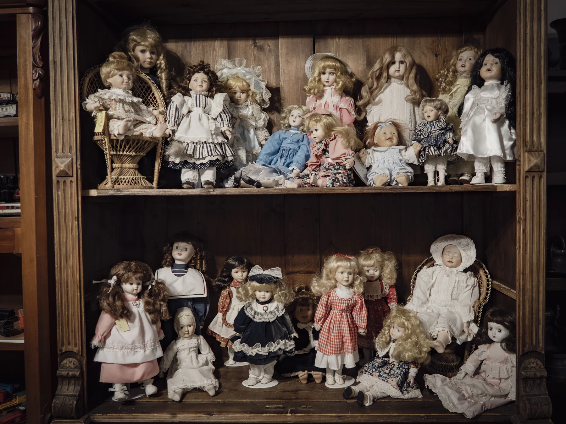 Two wooden cabinet shelves crowded with porcelain dolls in lace dresses