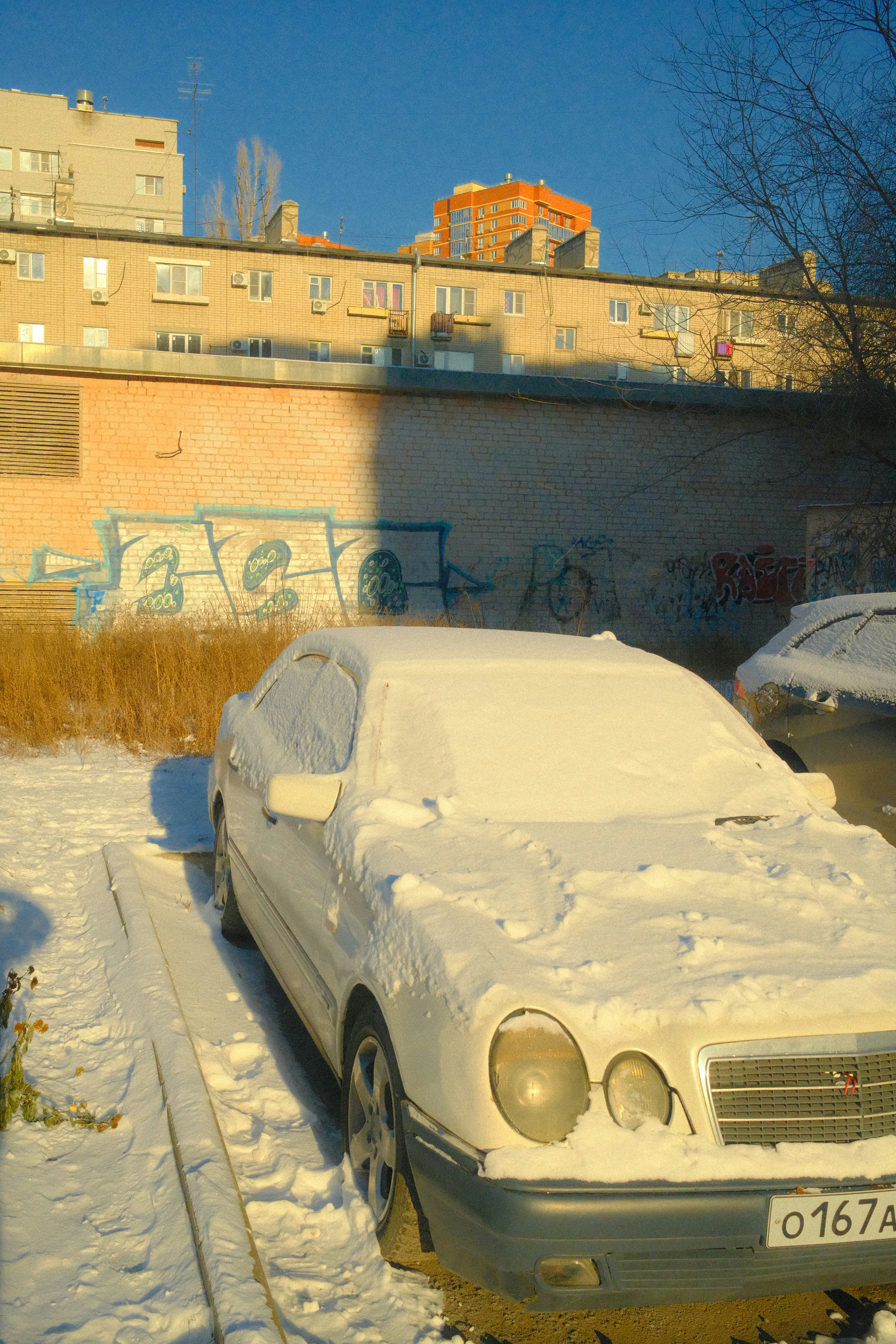 White car covered in snow with buildings behind.