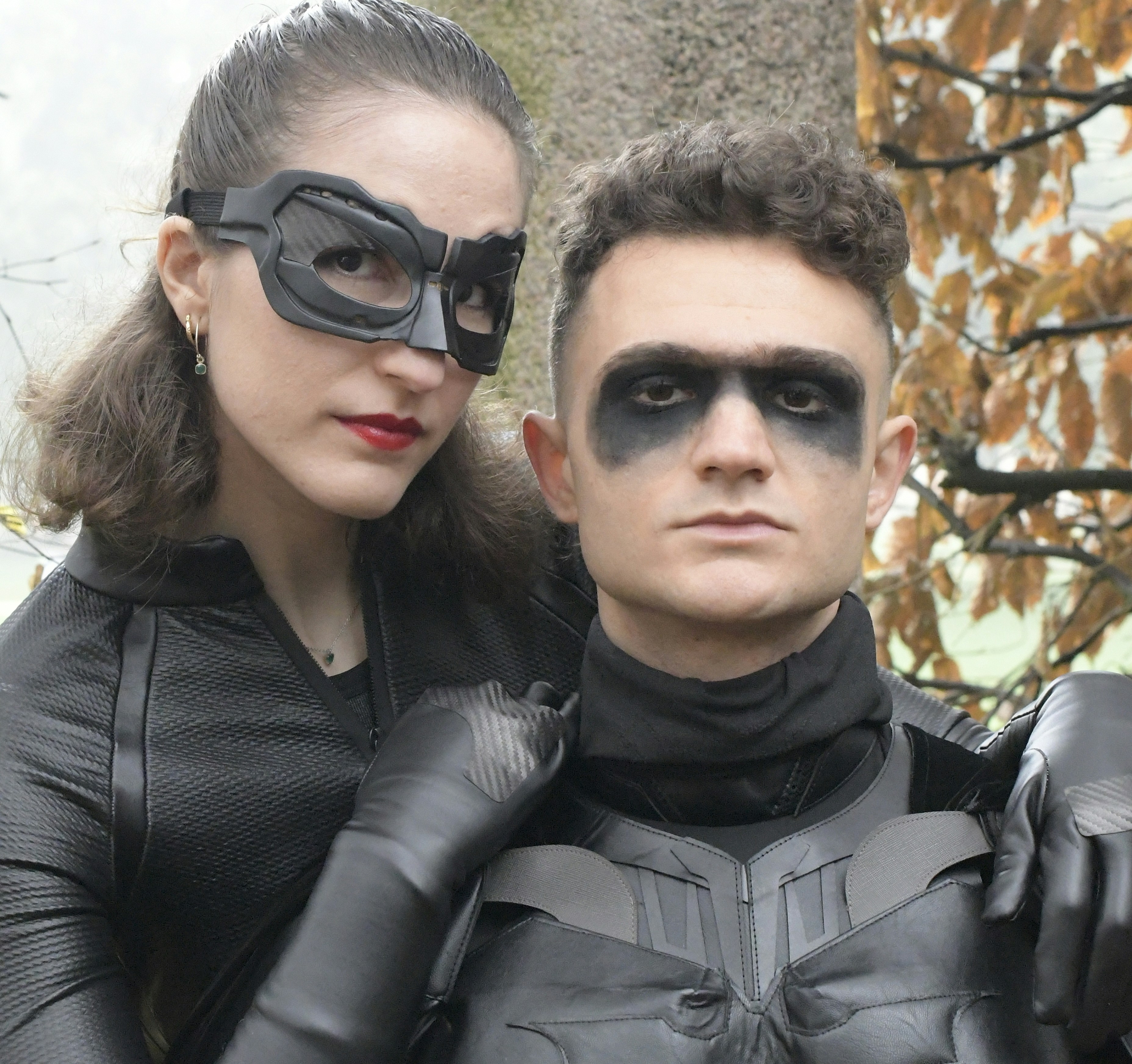 Couple dressed as batman and catwoman outdoors.