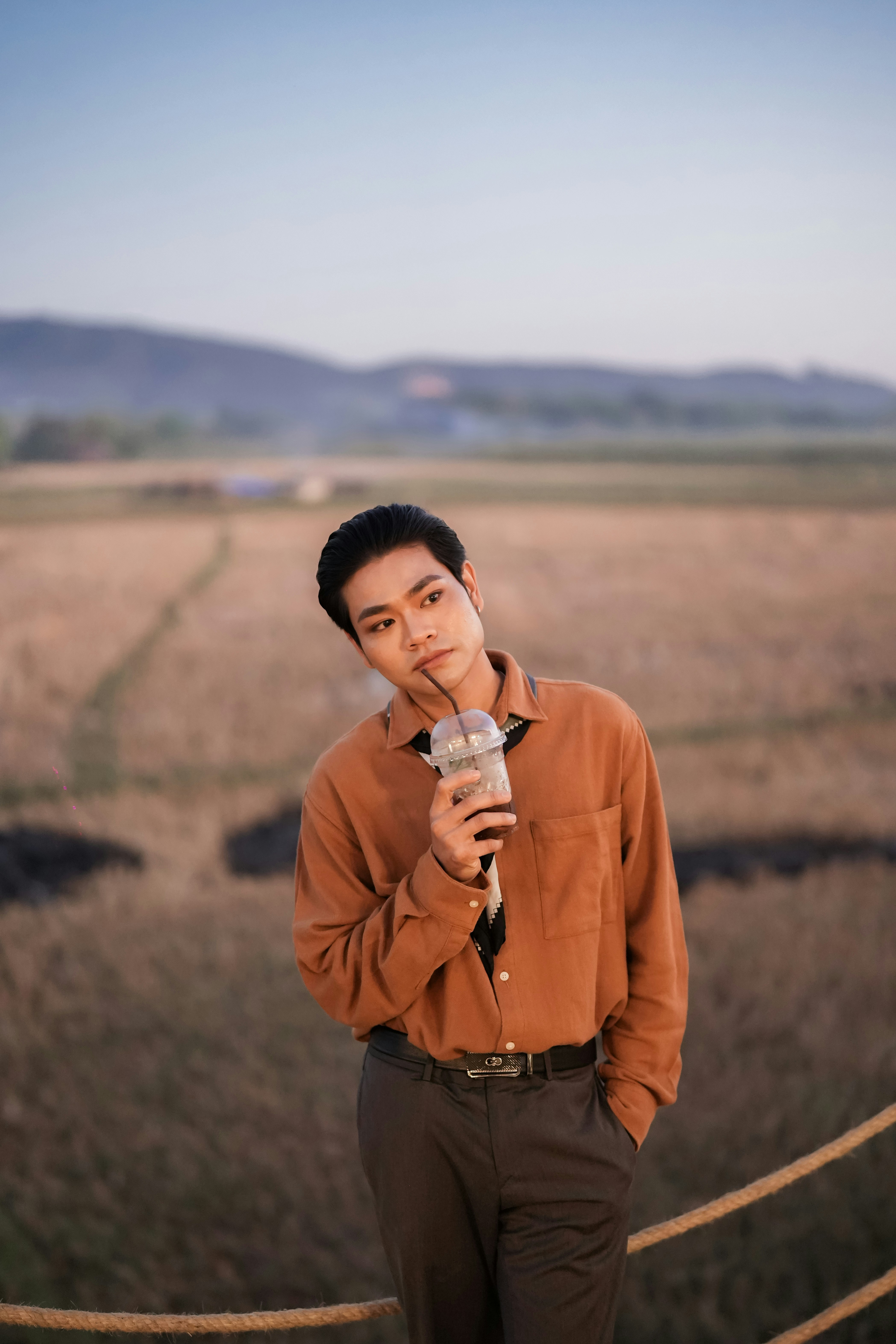 Joven con camisa marrón bebiendo de la taza al aire libre