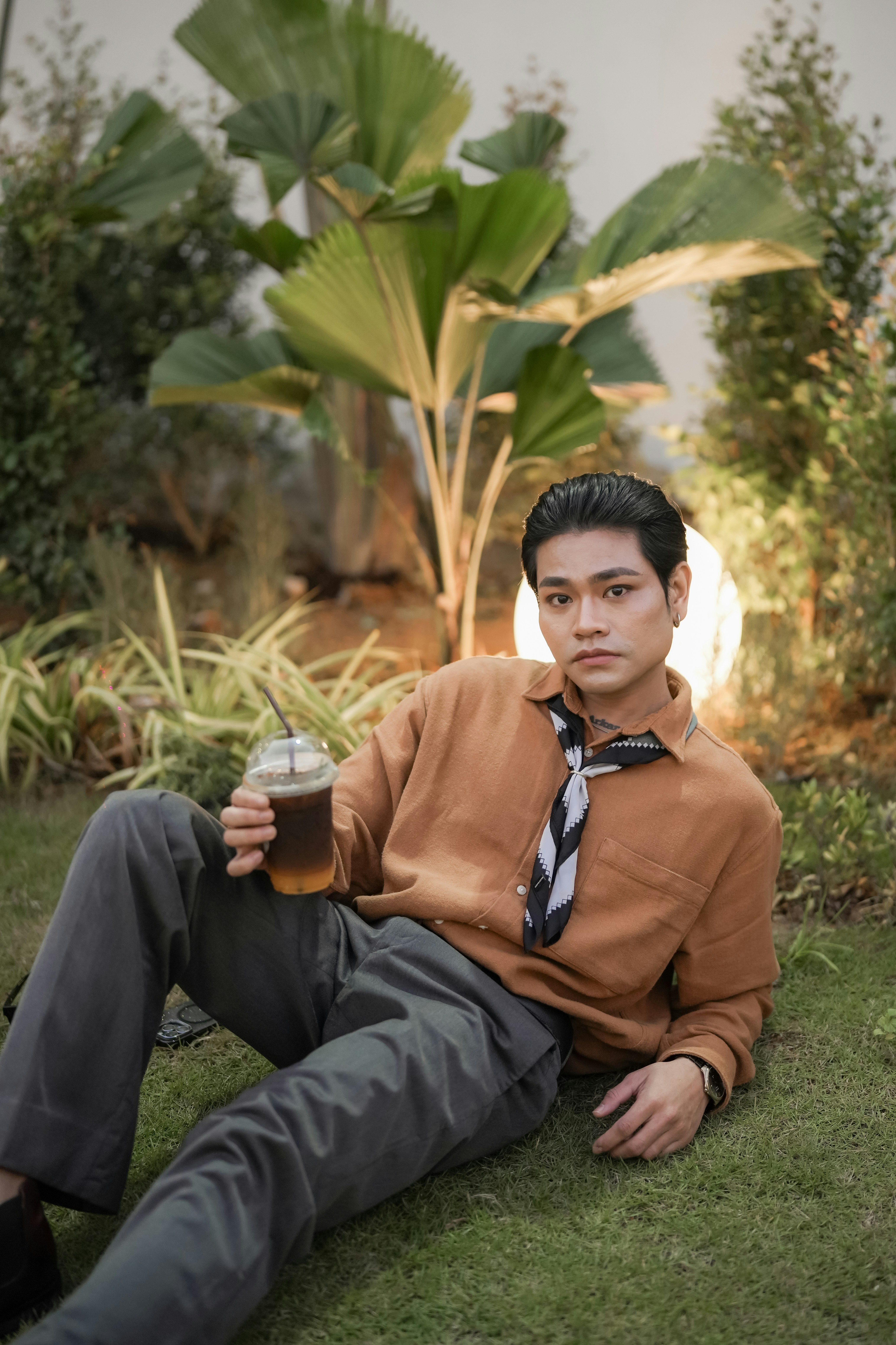 Man in a brown shirt holding iced coffee outdoors.