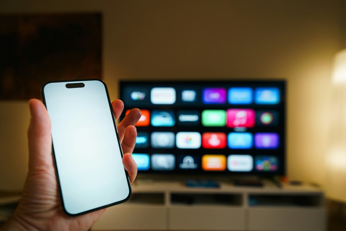 A smartphone held in front of a smart TV screen showing streaming platforms