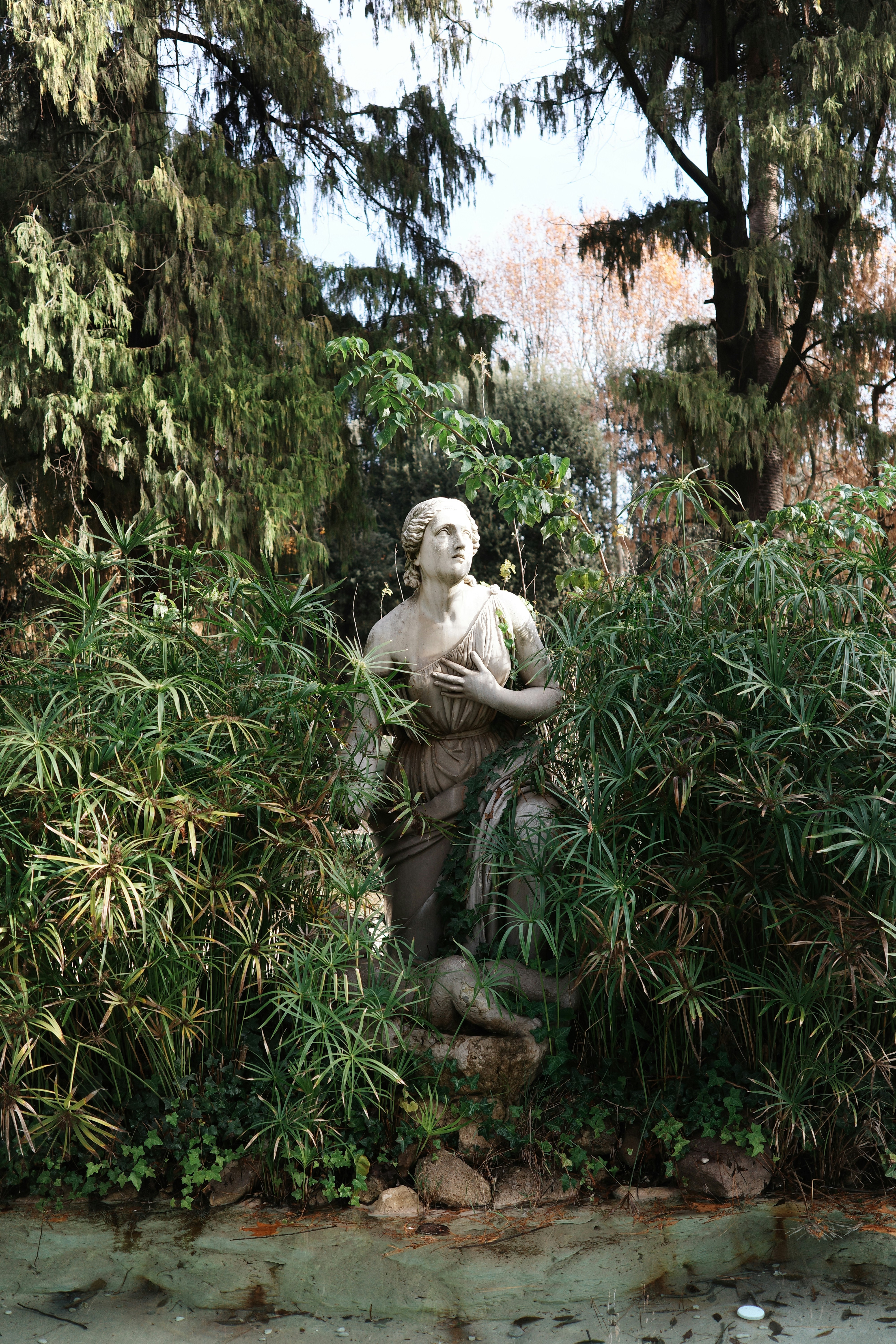 Stone statue of a woman in a lush garden.