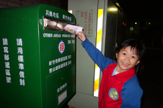 A child mailing a letter into a green mailbox.