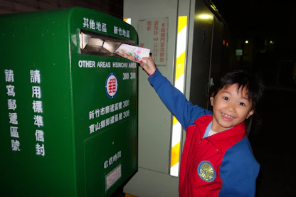 A child mailing a letter into a green mailbox.