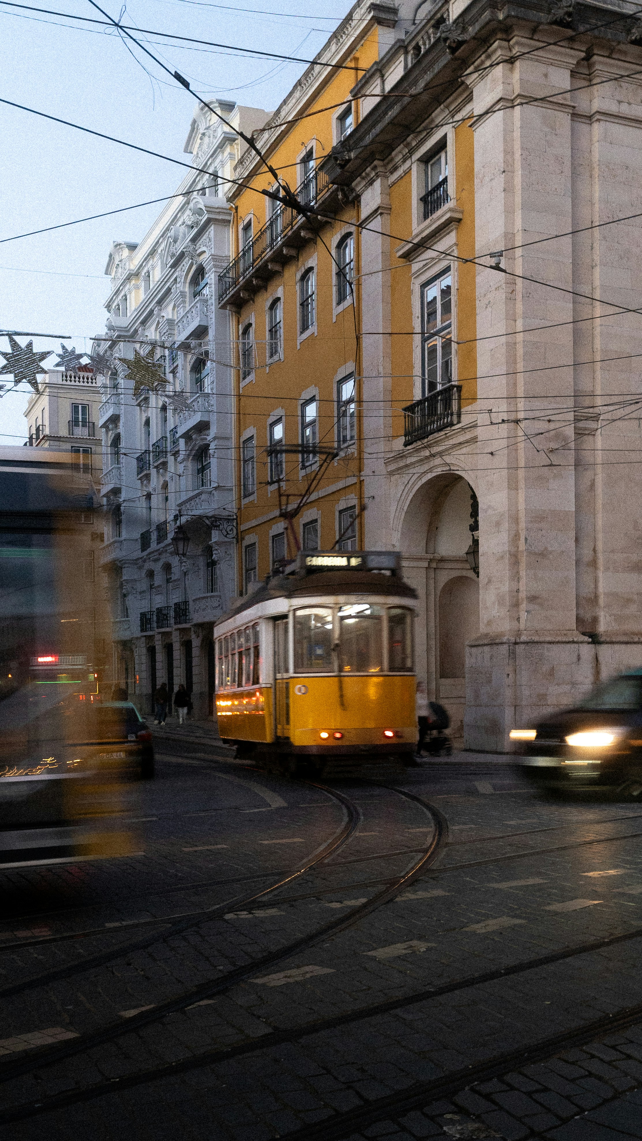 Yellow tram on city street with blurred vehicles.