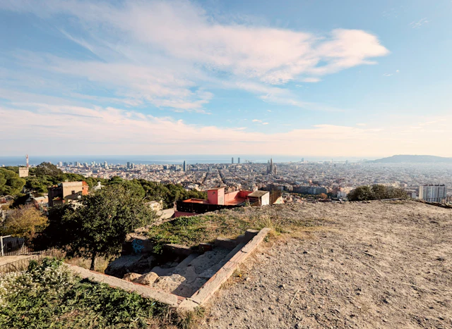 The rough, open hilltop of Bunkers del Carmel with low wall remnants and Barcelona's skyline spread out below