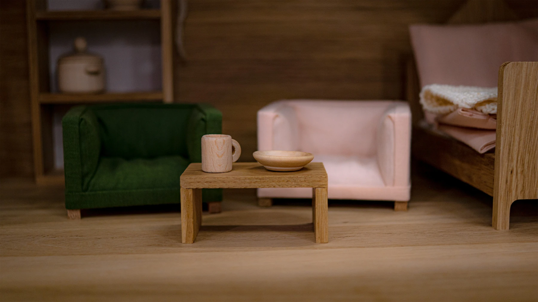 A green and a pink miniature armchair around a wooden coffee table holding a tiny mug and bowl