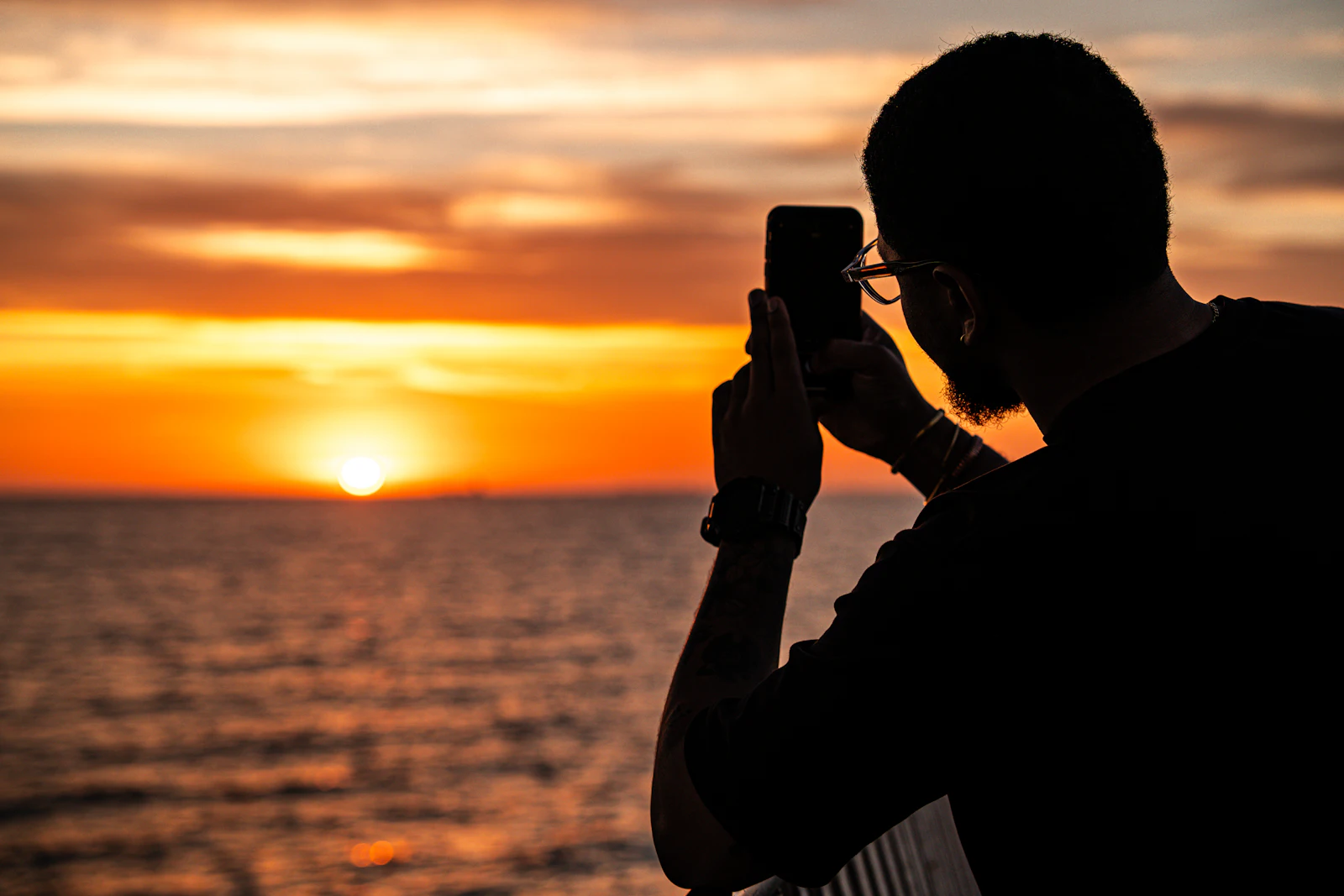 Traveller filming a sunset over the sea on a smartphone, a video upload that uses far more travel data than photos