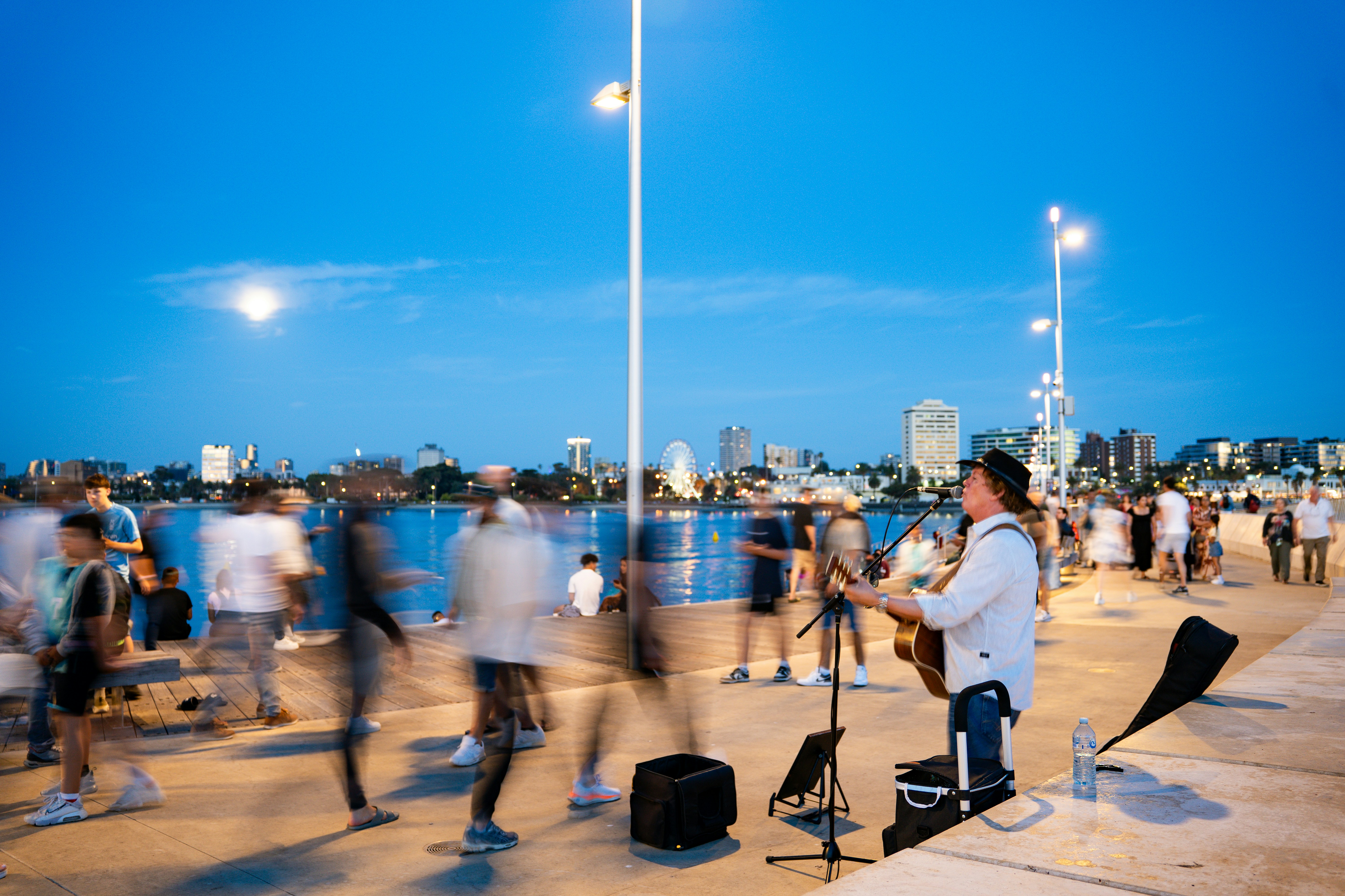 Musician plays guitar on waterfront promenade at dusk