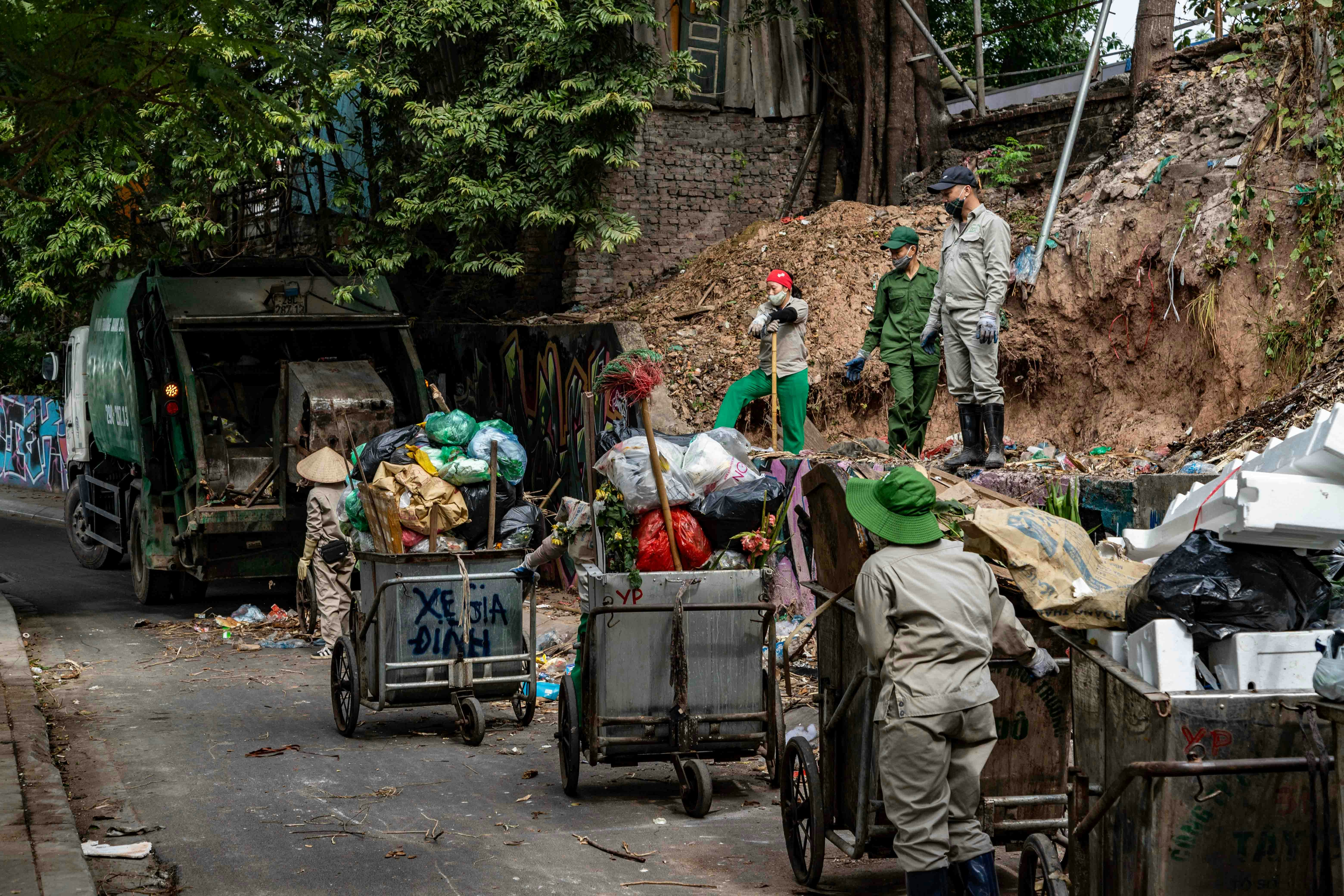 Workers collect trash with a garbage truck and carts.