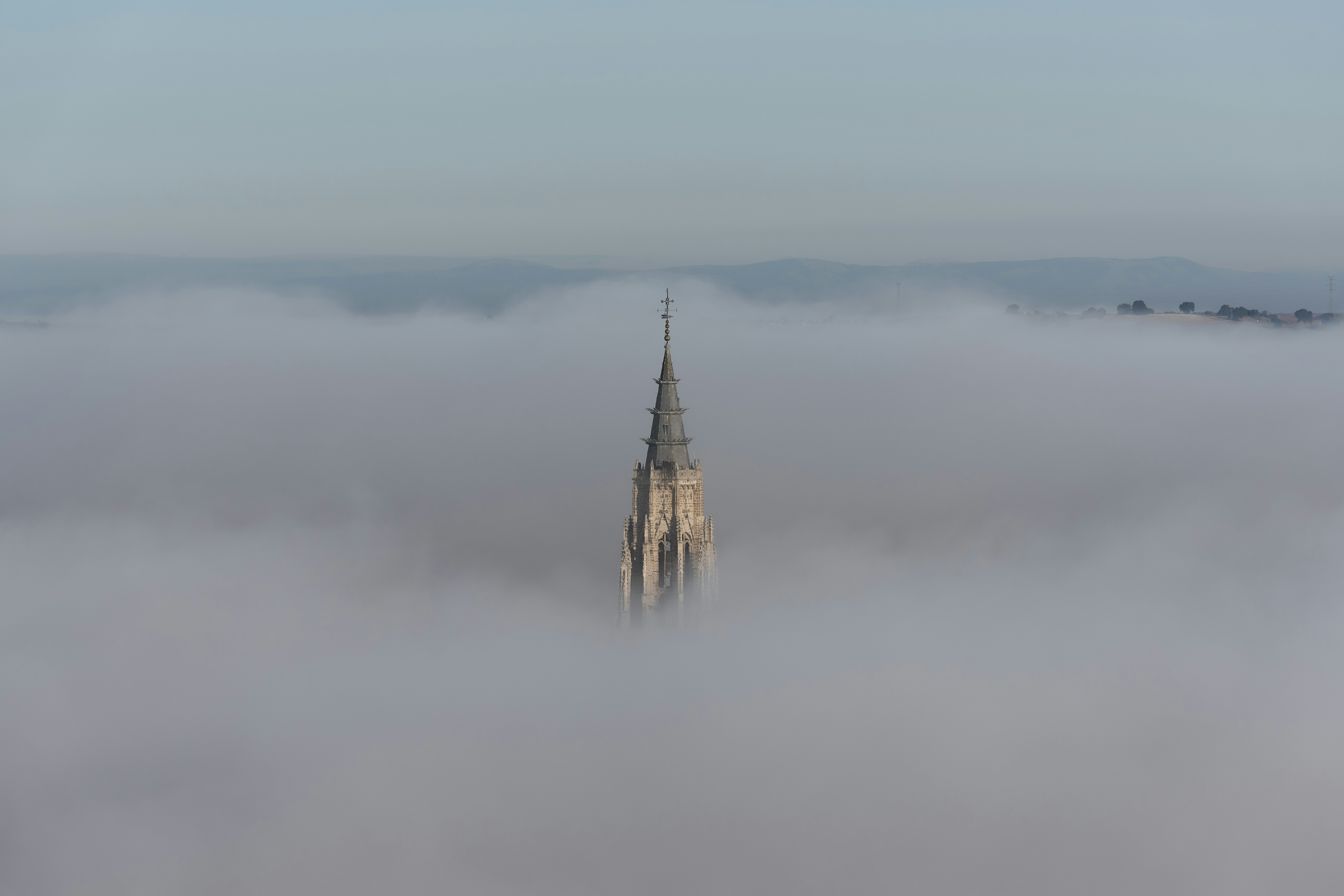 Um campanário de igreja emerge de uma névoa densa.