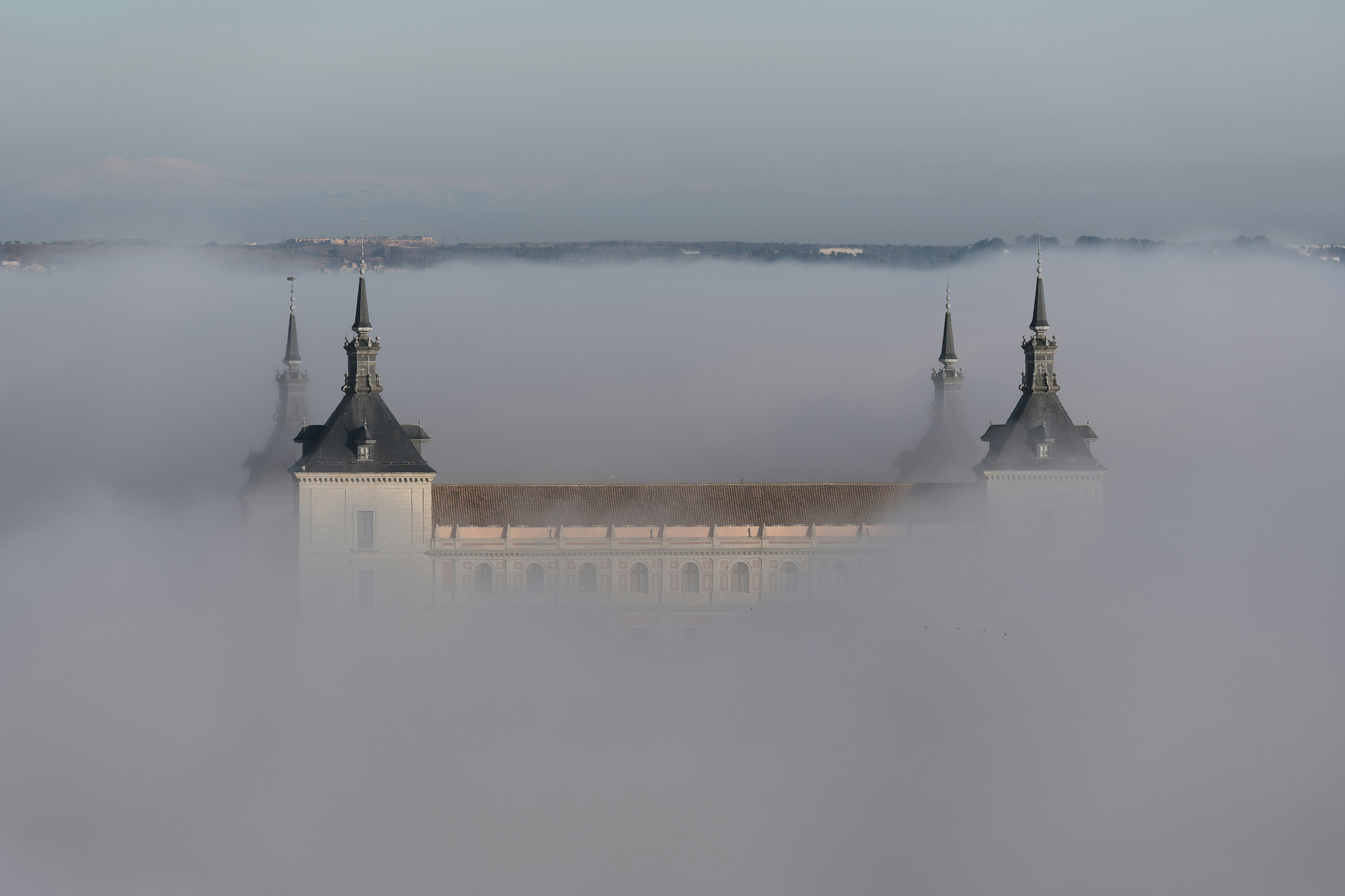 Torres do castelo emergem de uma névoa densa sob um céu pálido.