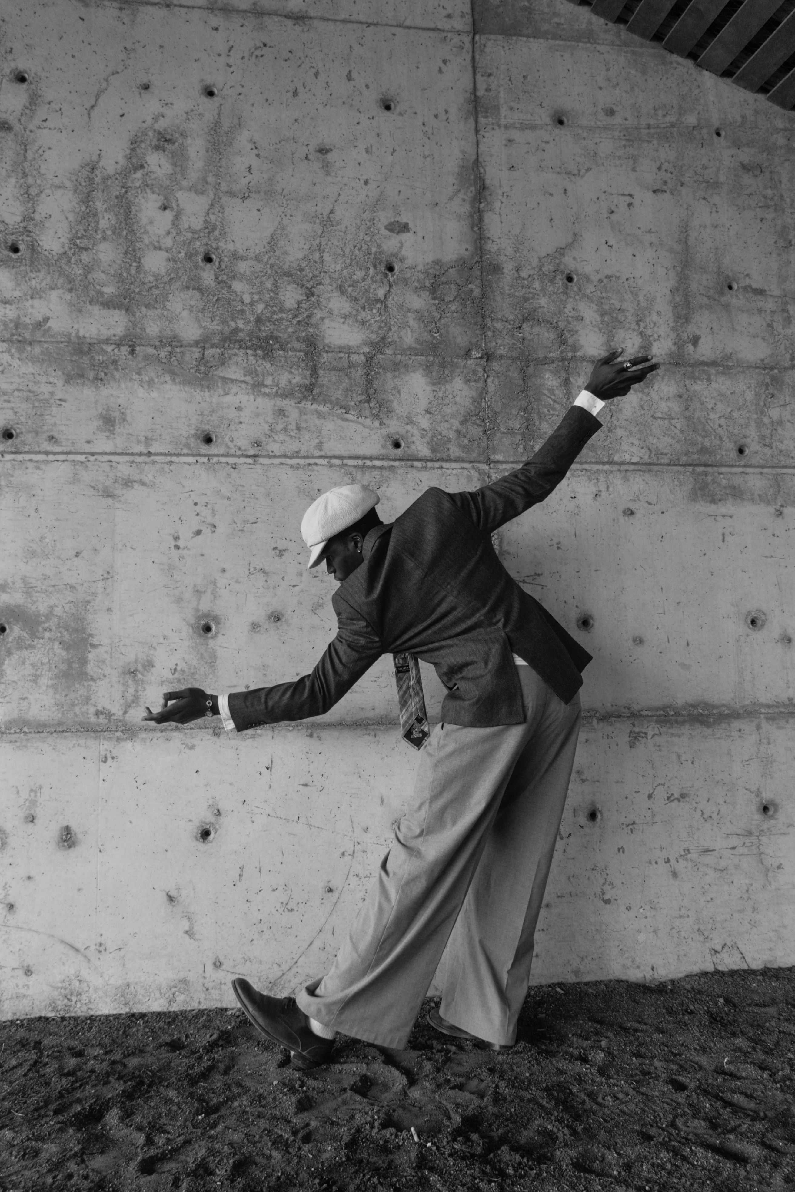 Un homme en costume et chapeau danse contre un mur en béton
