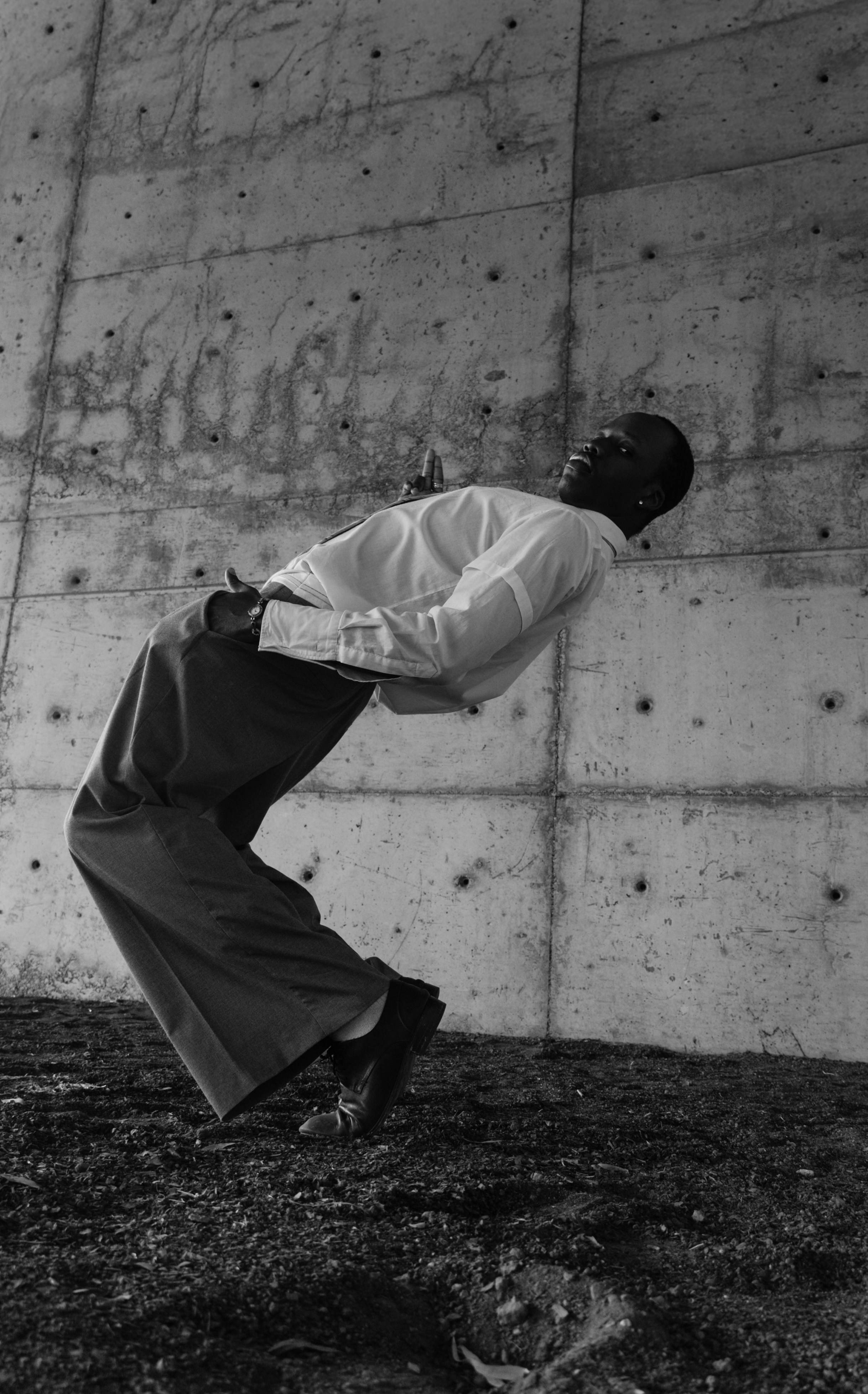 Homme en chemise blanche penché en arrière contre un mur en béton