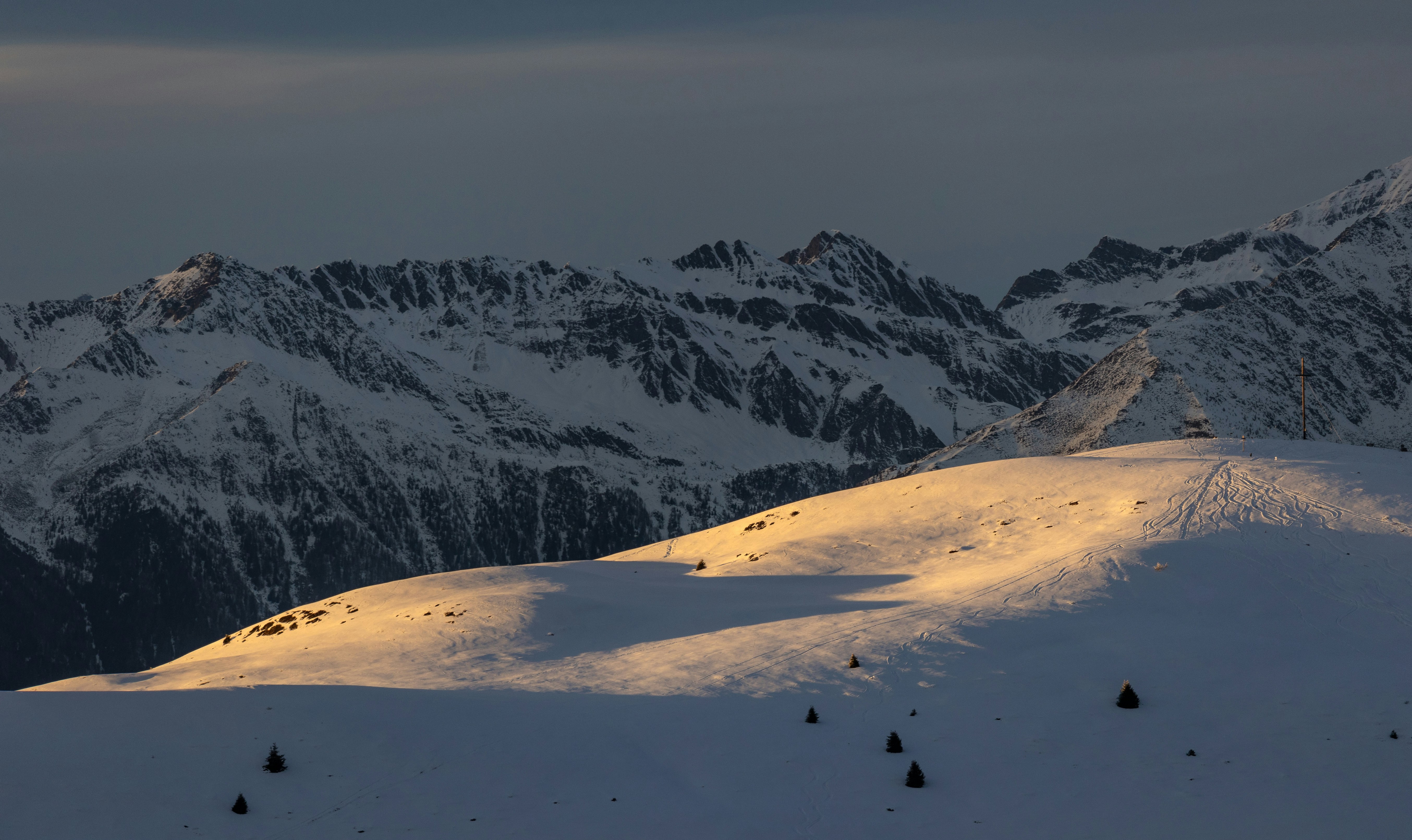 Golden sunlight illuminates snow-covered mountain peaks at dusk.