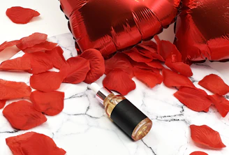 Red heart balloons and rose petals with a bottle.