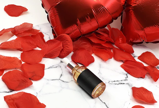 Red heart balloons and rose petals with a bottle.
