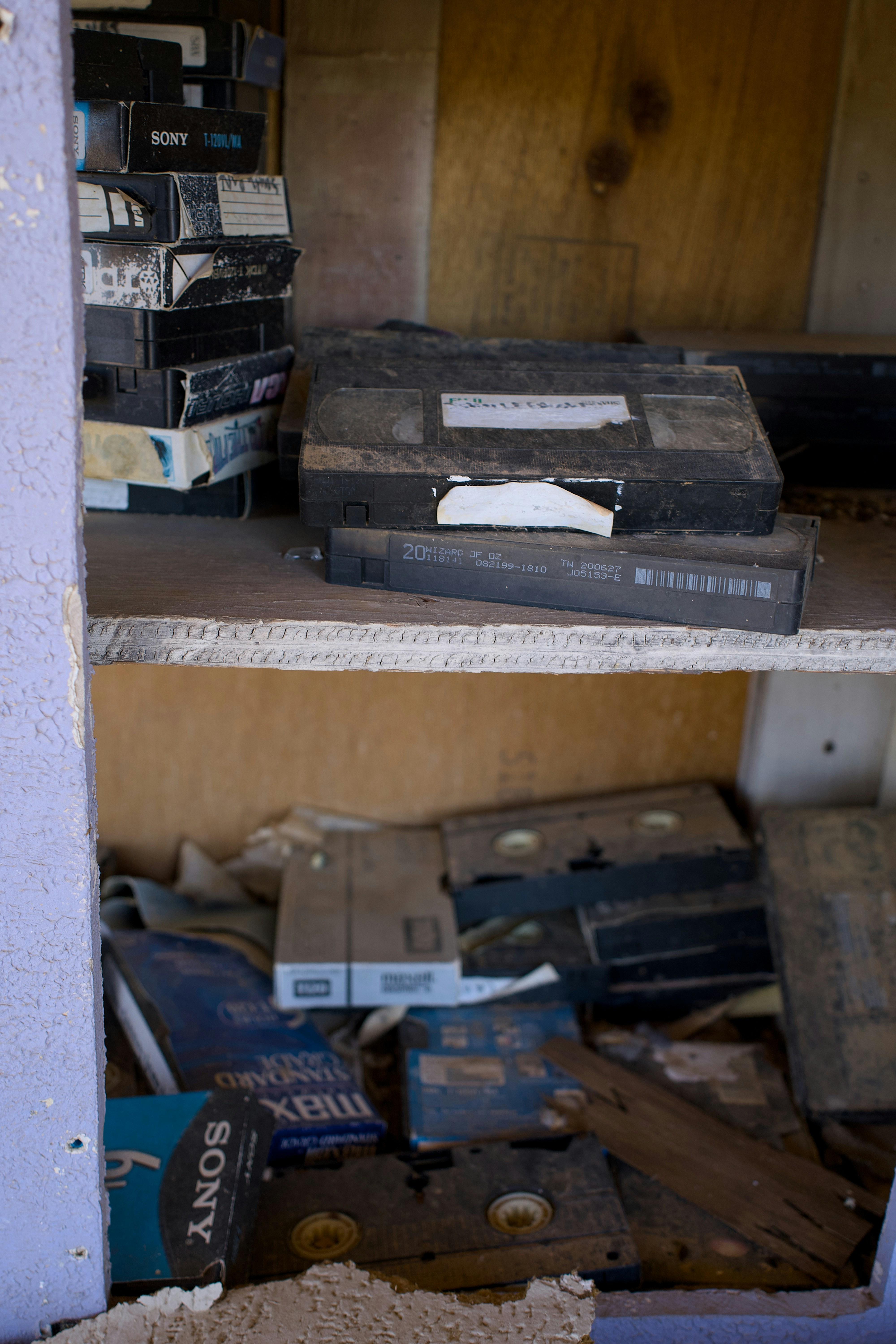 Dusty vhs tapes stacked on shelves in a shelf.