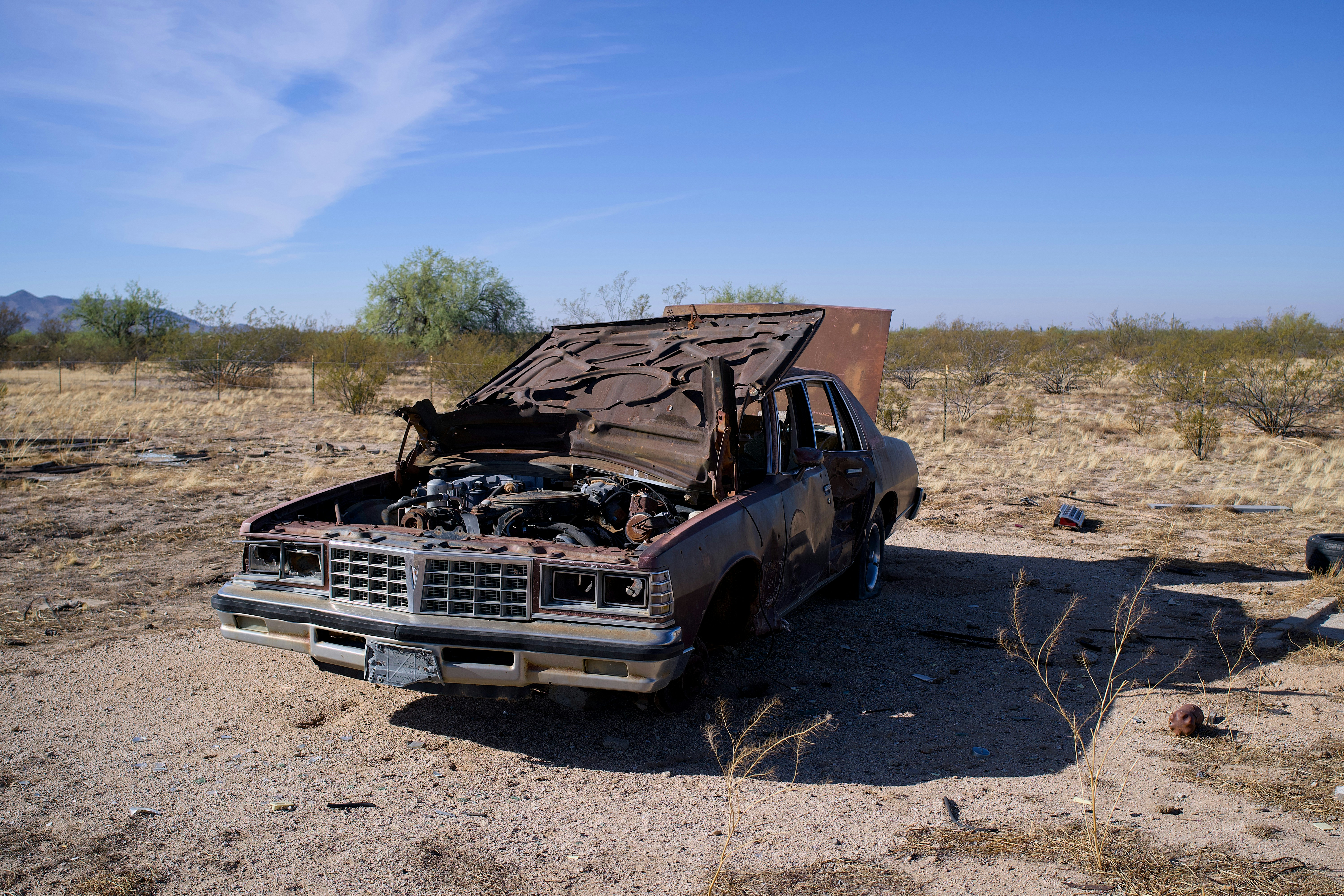 Abandoned rusty car in a dry, desolate landscape.