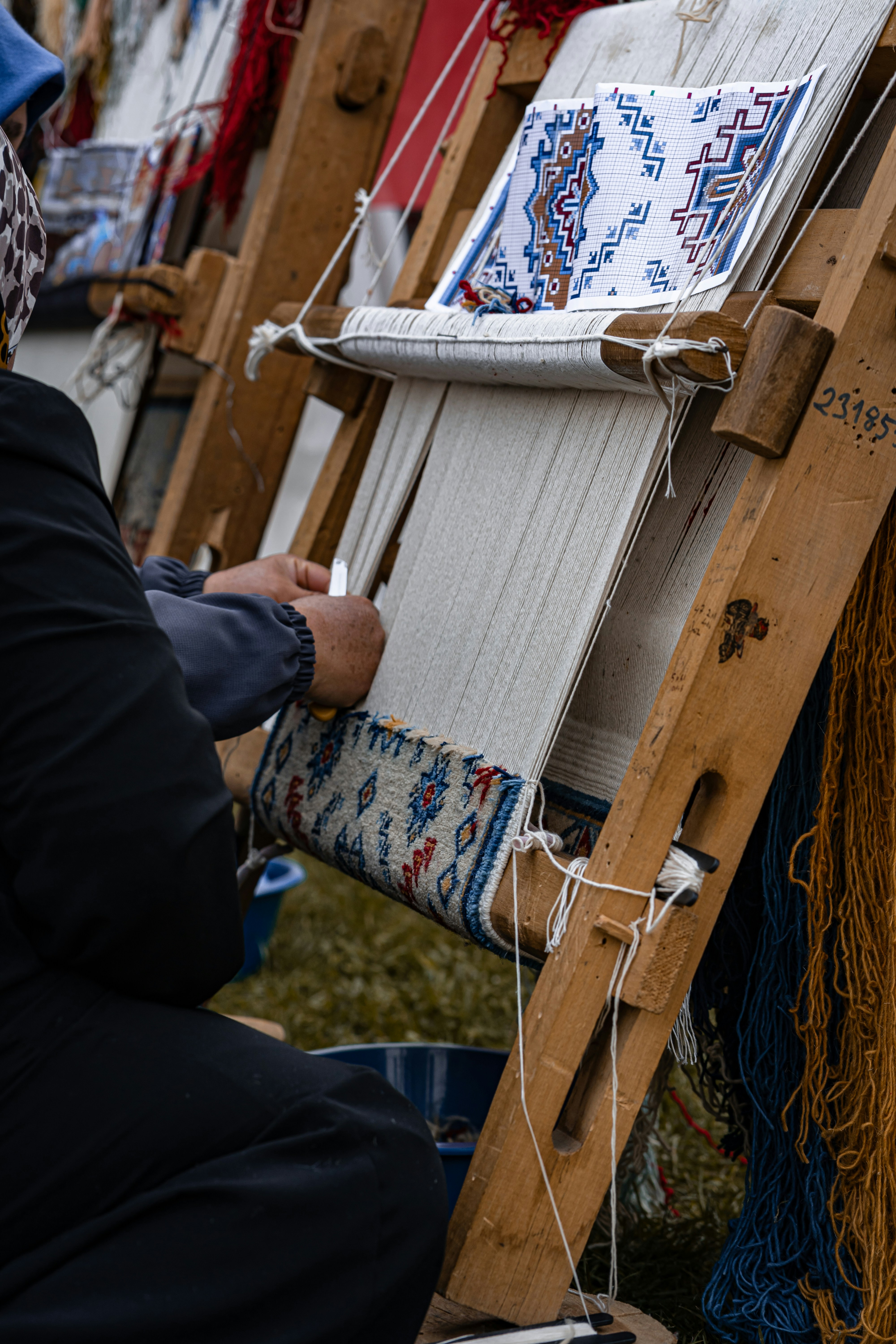 Person weaving a colorful patterned rug on a loom.