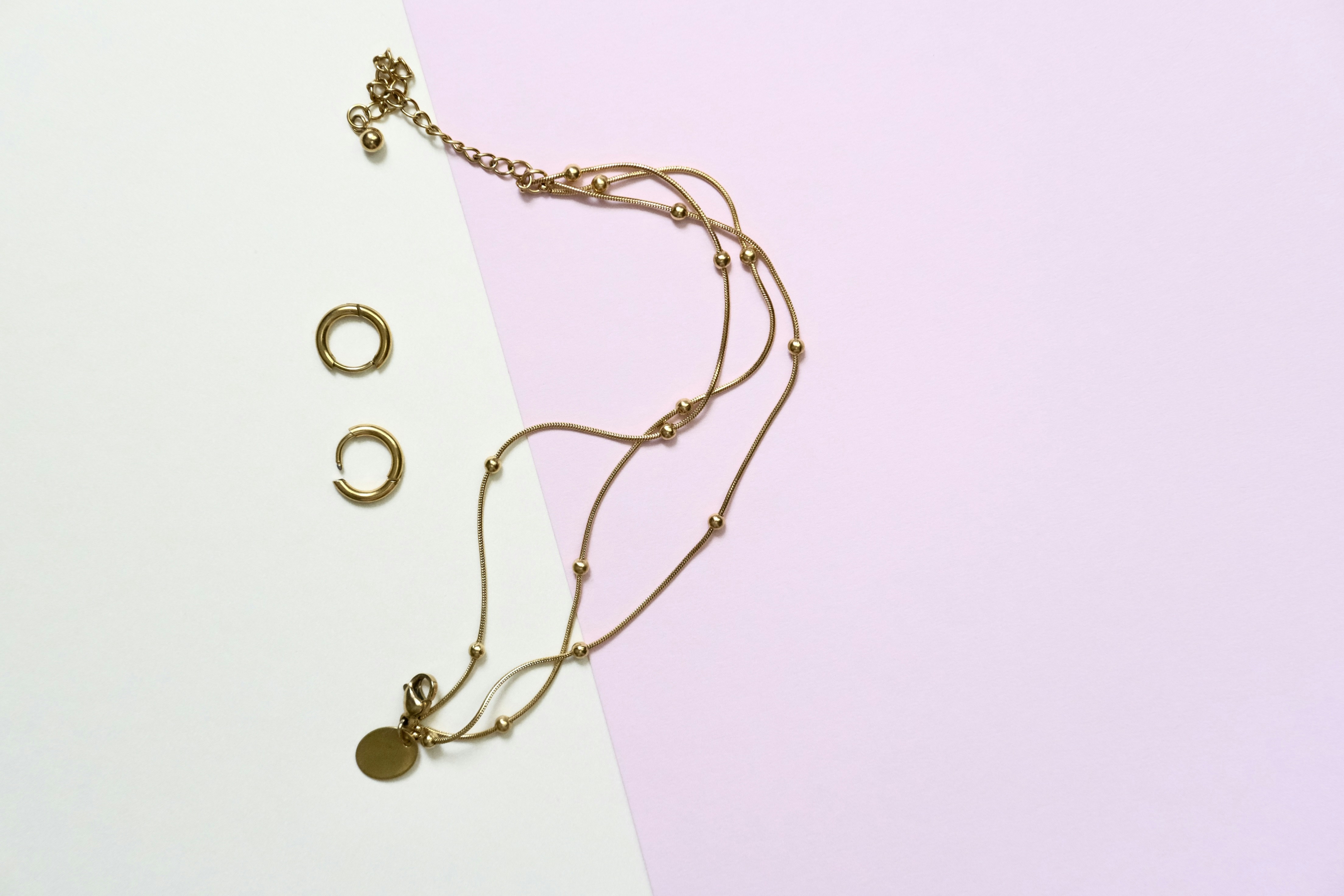 Gold necklace and earrings on pastel background.