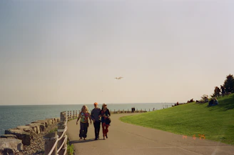 Three people walk along a seaside path.