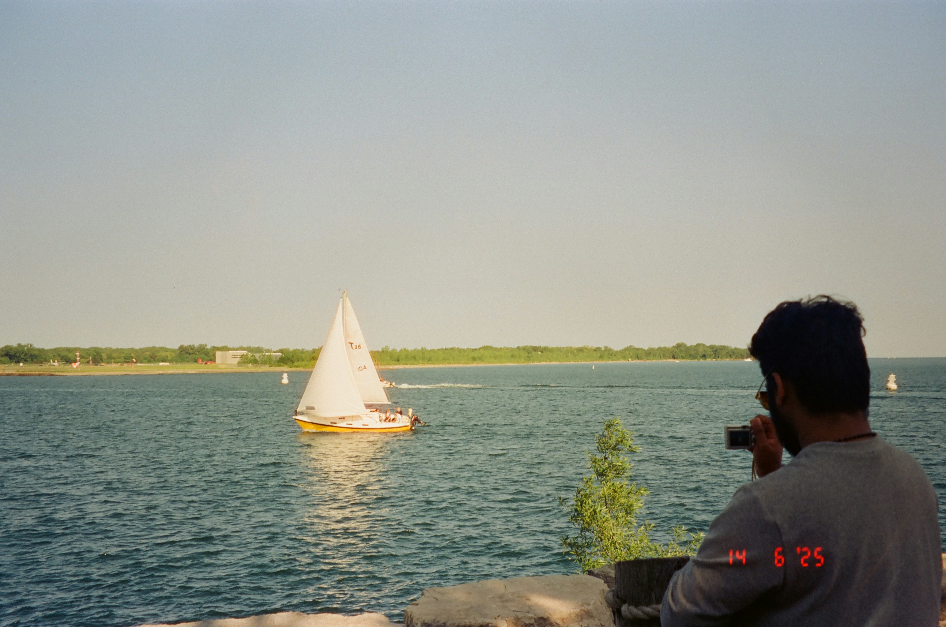 Man photographs sailboat on a sunny day.