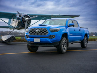Blue pickup truck parked next to an airplane.