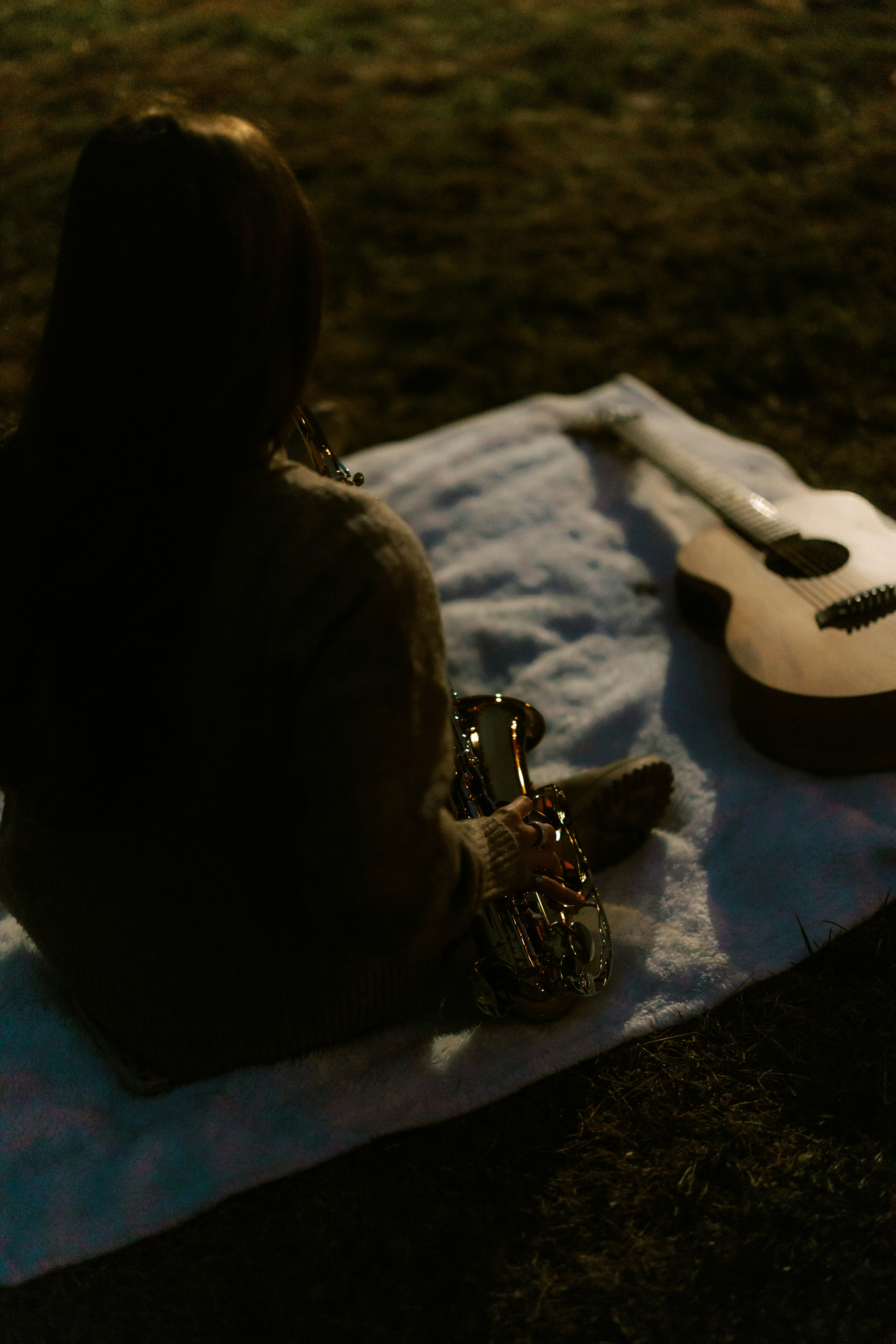 Person with saxophone and guitar on blanket.