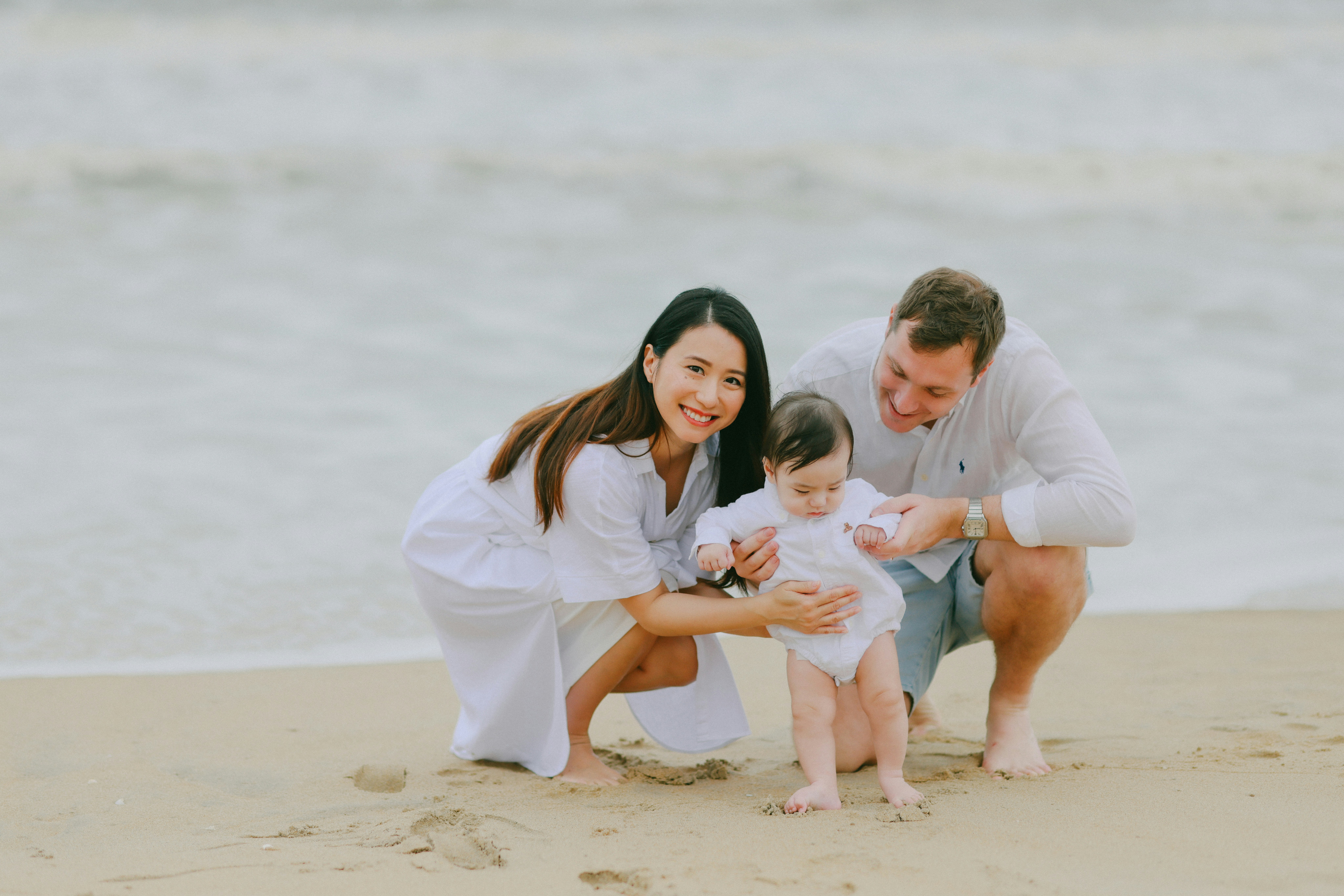 Family posing on a sandy beach near the ocean.