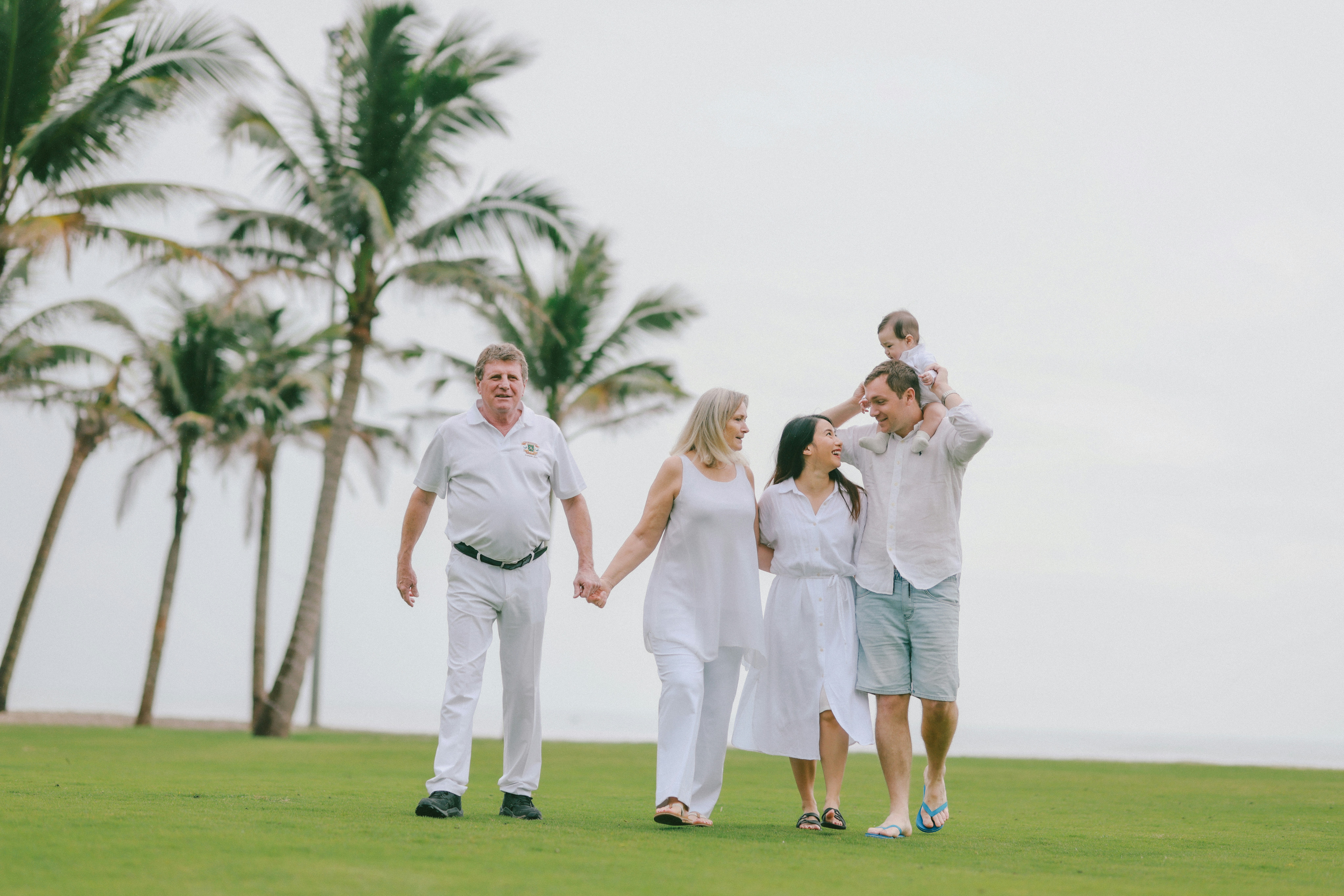Eine Familie geht Hand in Hand über einen grasbewachsenen Rasen.