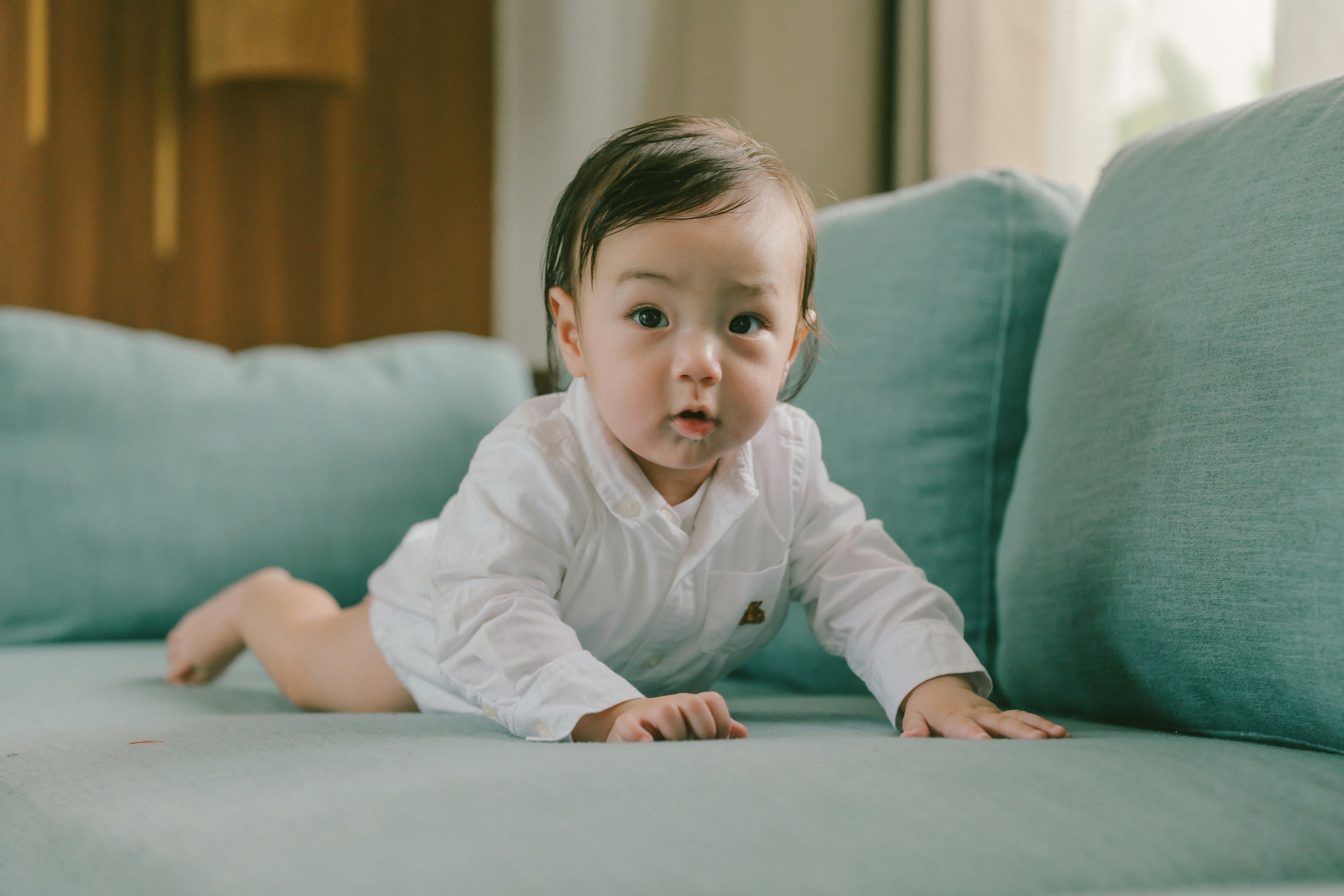 A baby in a white shirt crawls on a sofa.