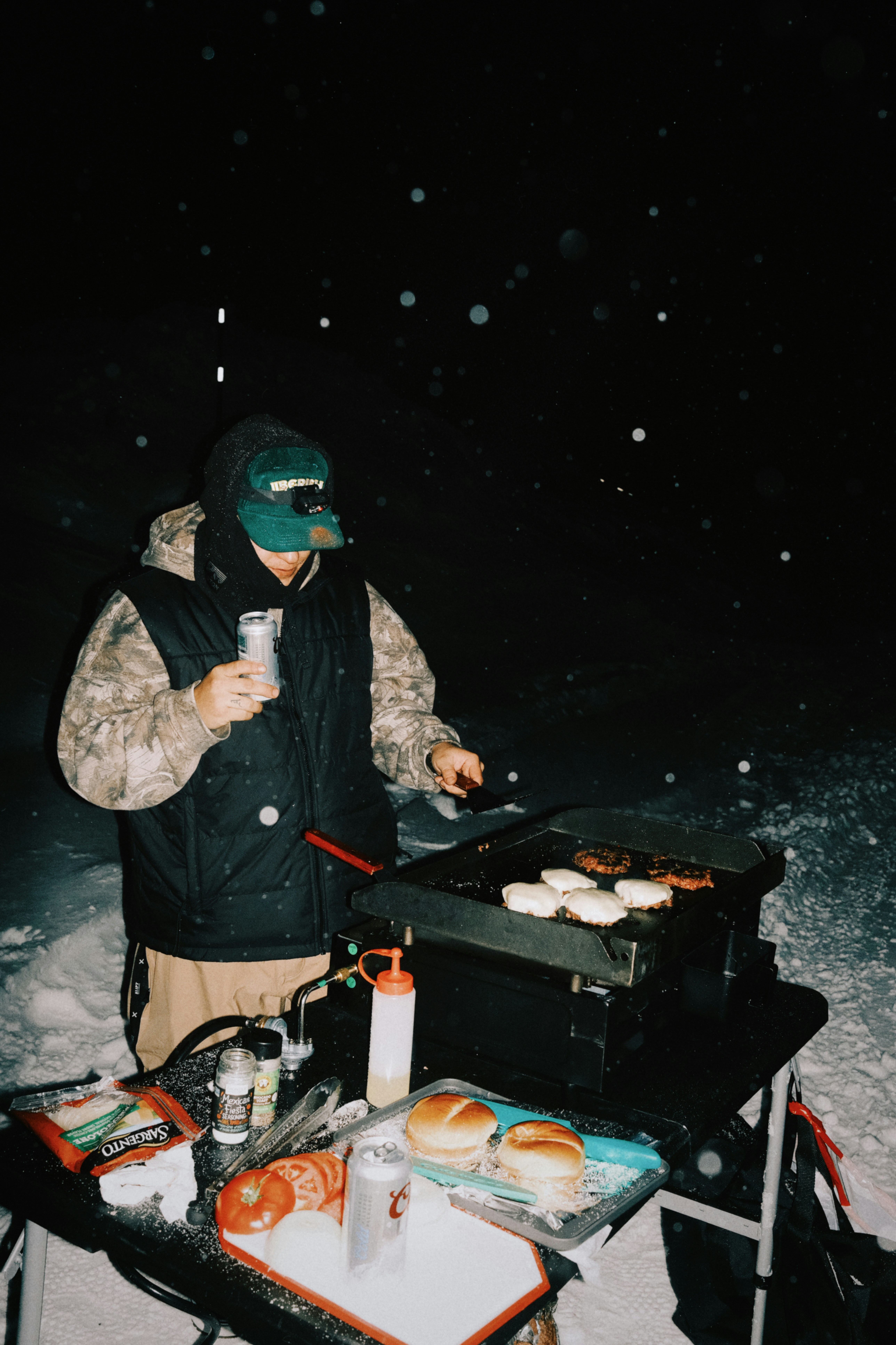 Person grilling burgers in the snow at night