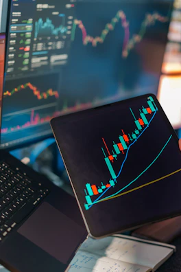 Trading charts displayed on multiple screens and tablet.