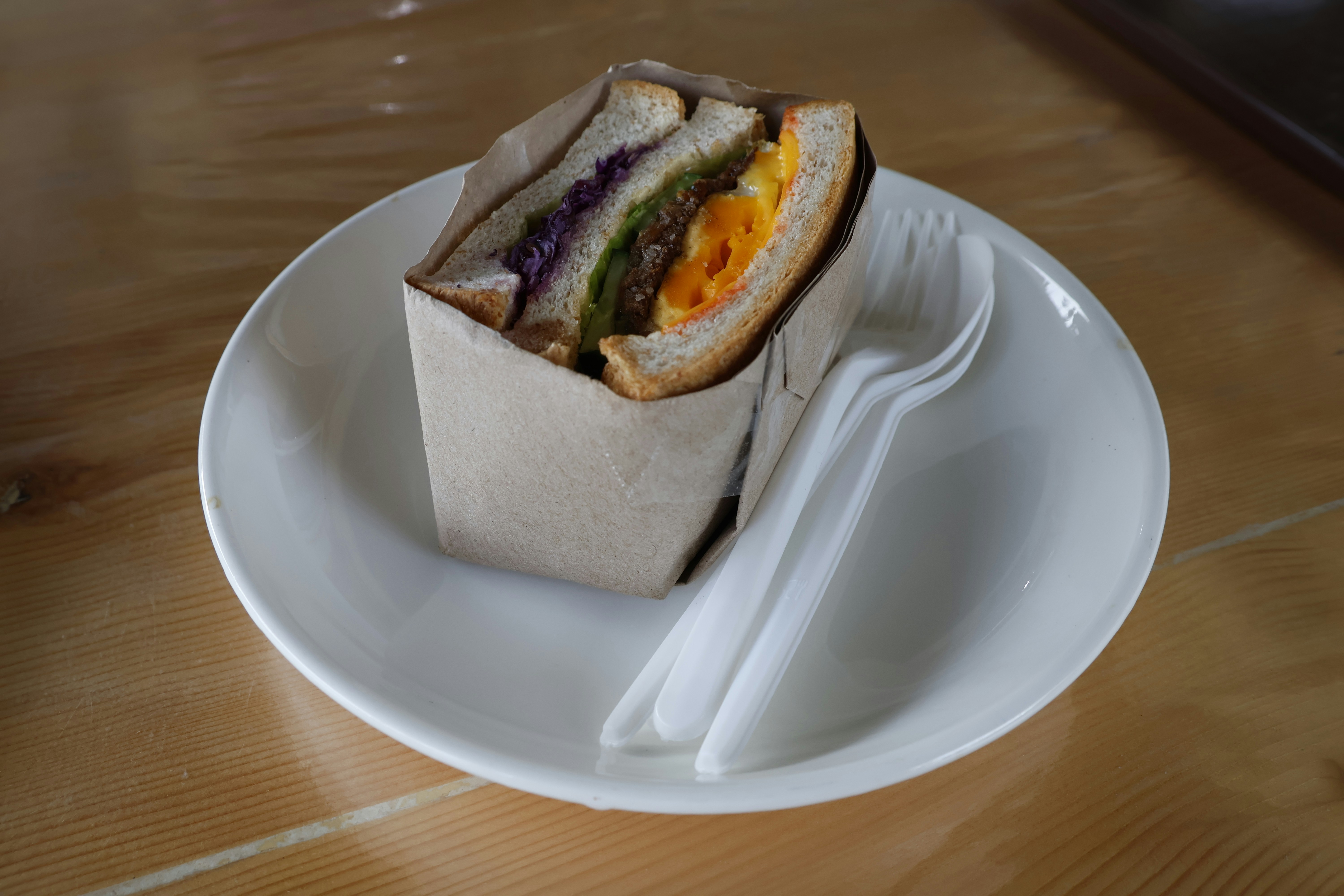 A sandwich wrapped in paper on a white plate.
