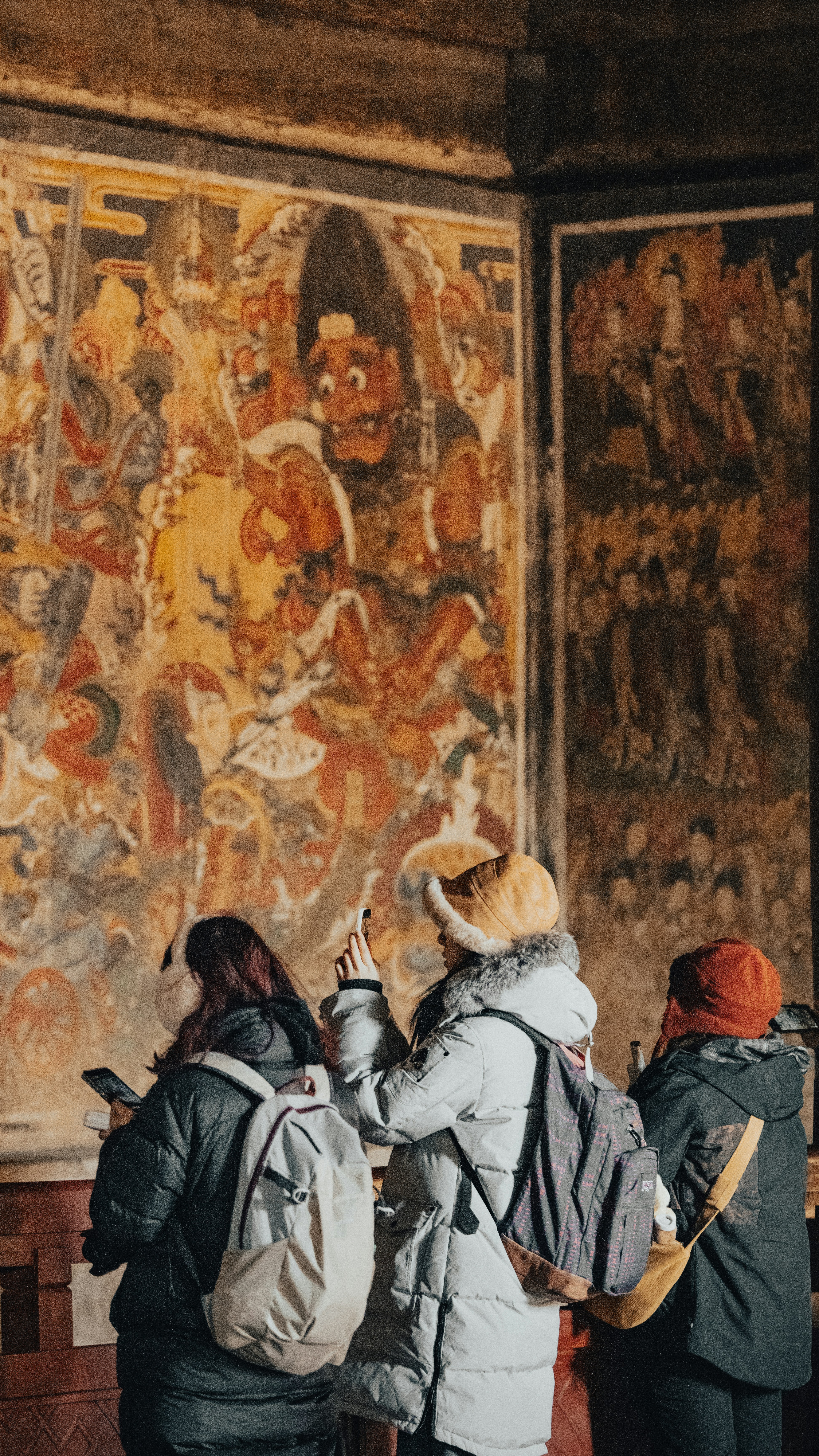People observe ancient murals inside a building.