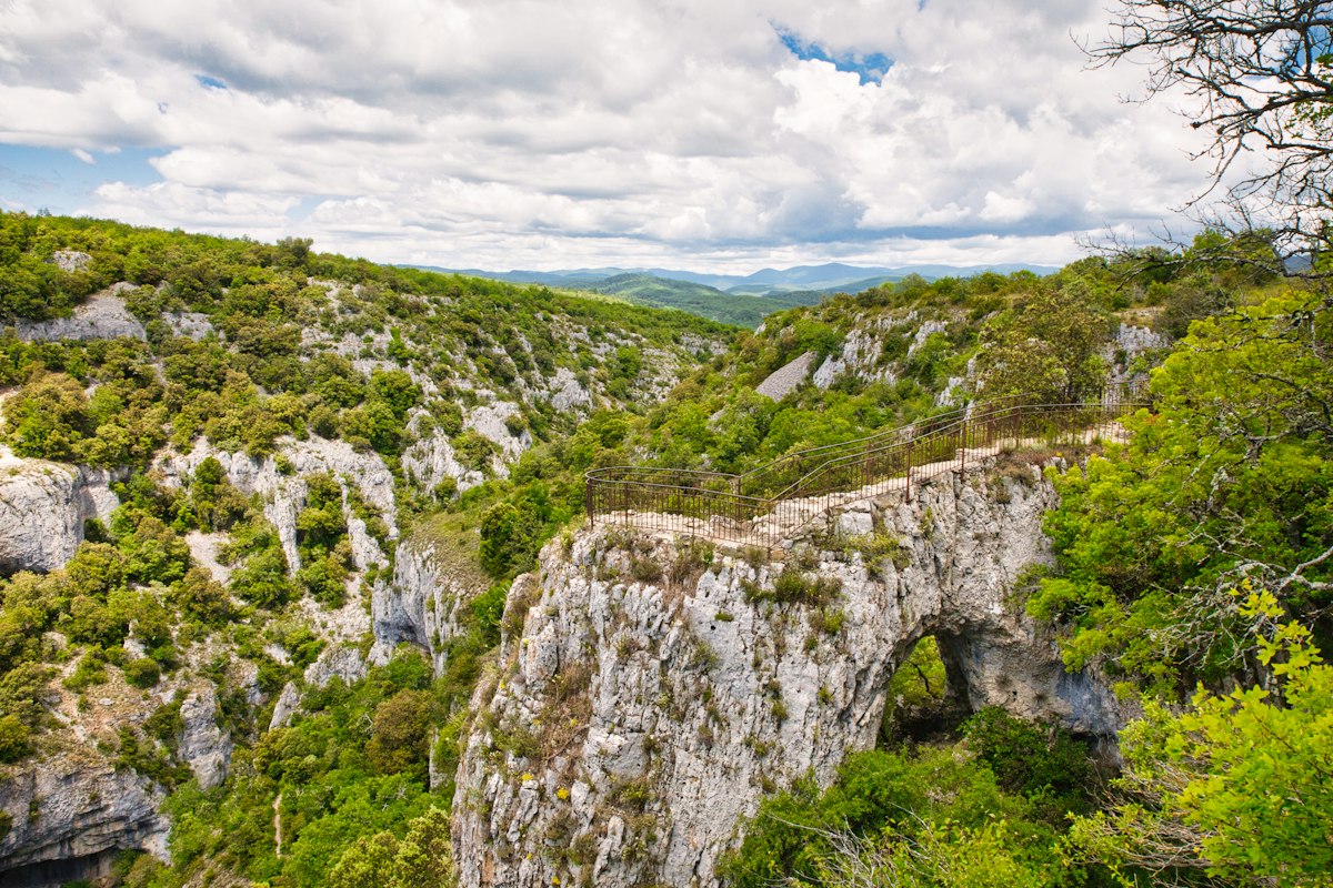 Green rocky gorge with a natural stone arch bridge