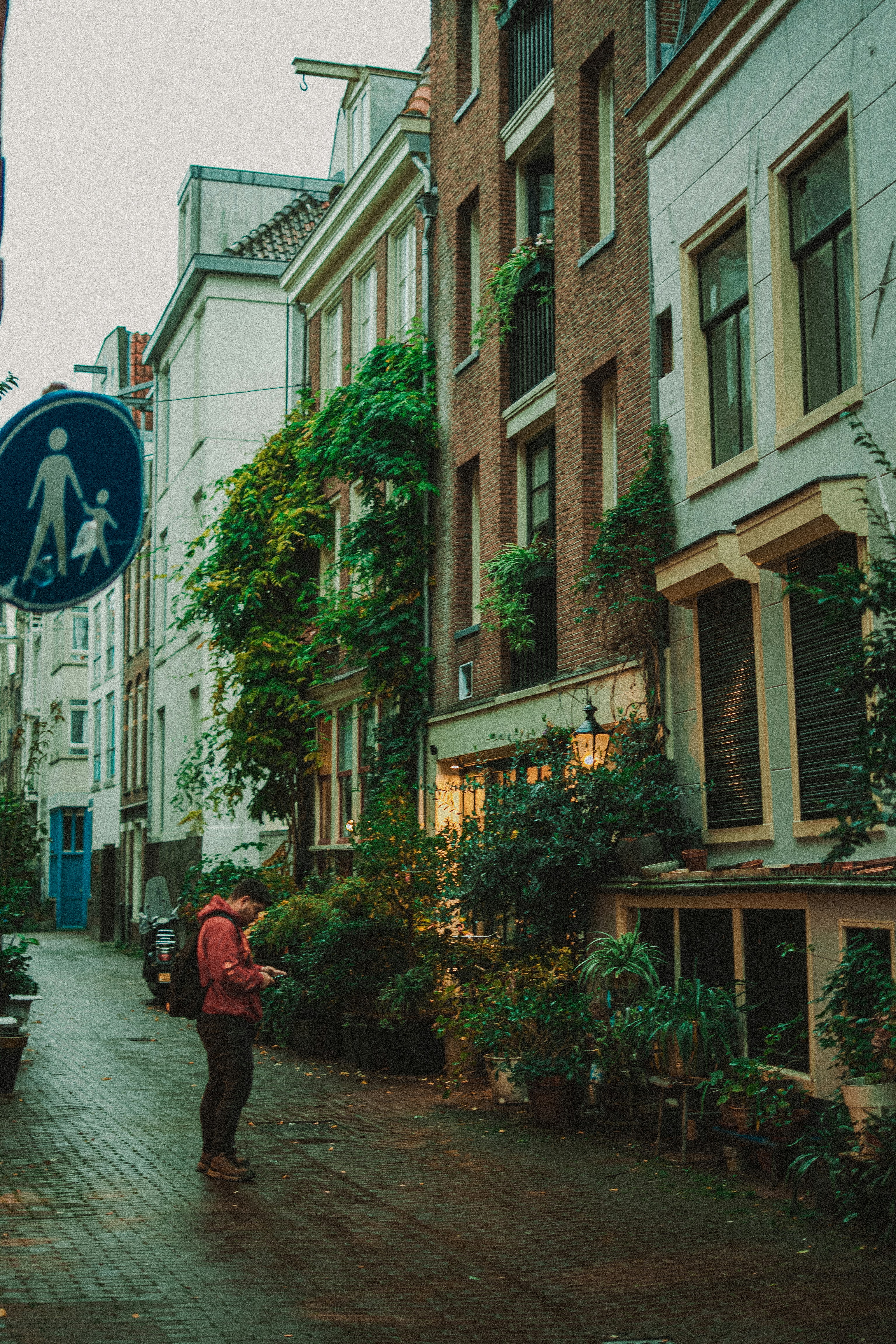Homem olhando para o celular numa rua de paralelepípedo molhada.