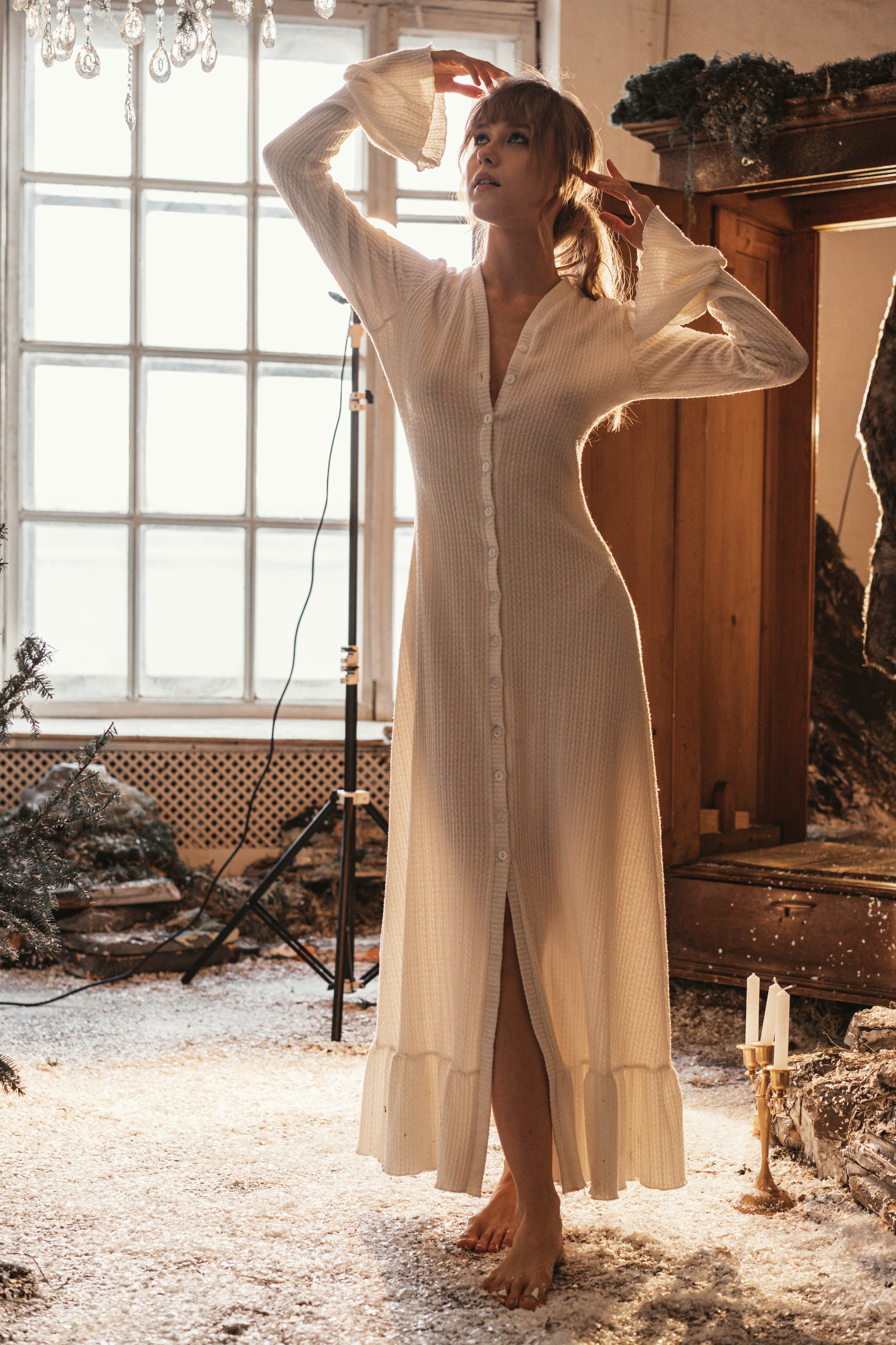 Woman in a white dress poses near a window.