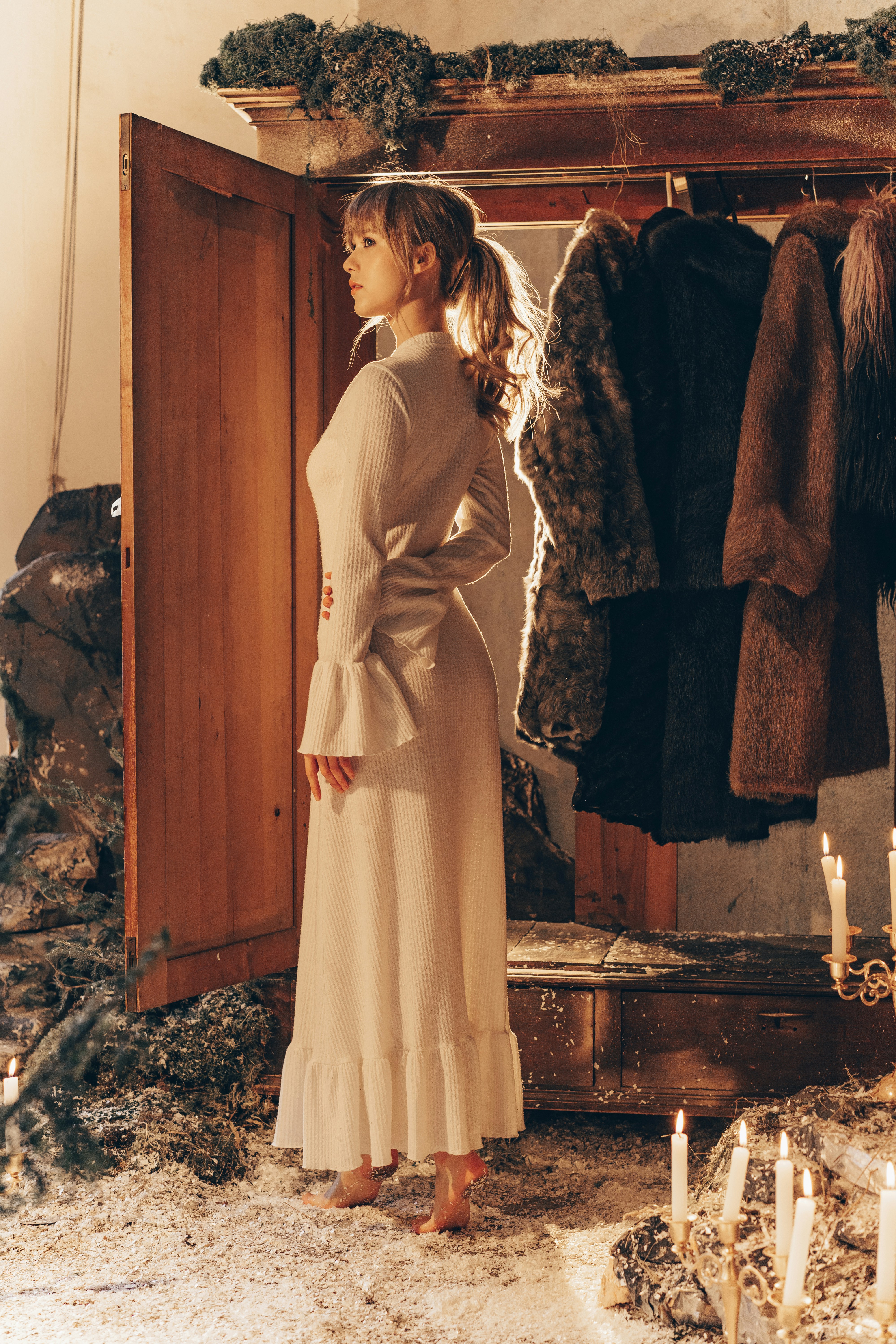 Woman in white dress by open wardrobe with fur coats