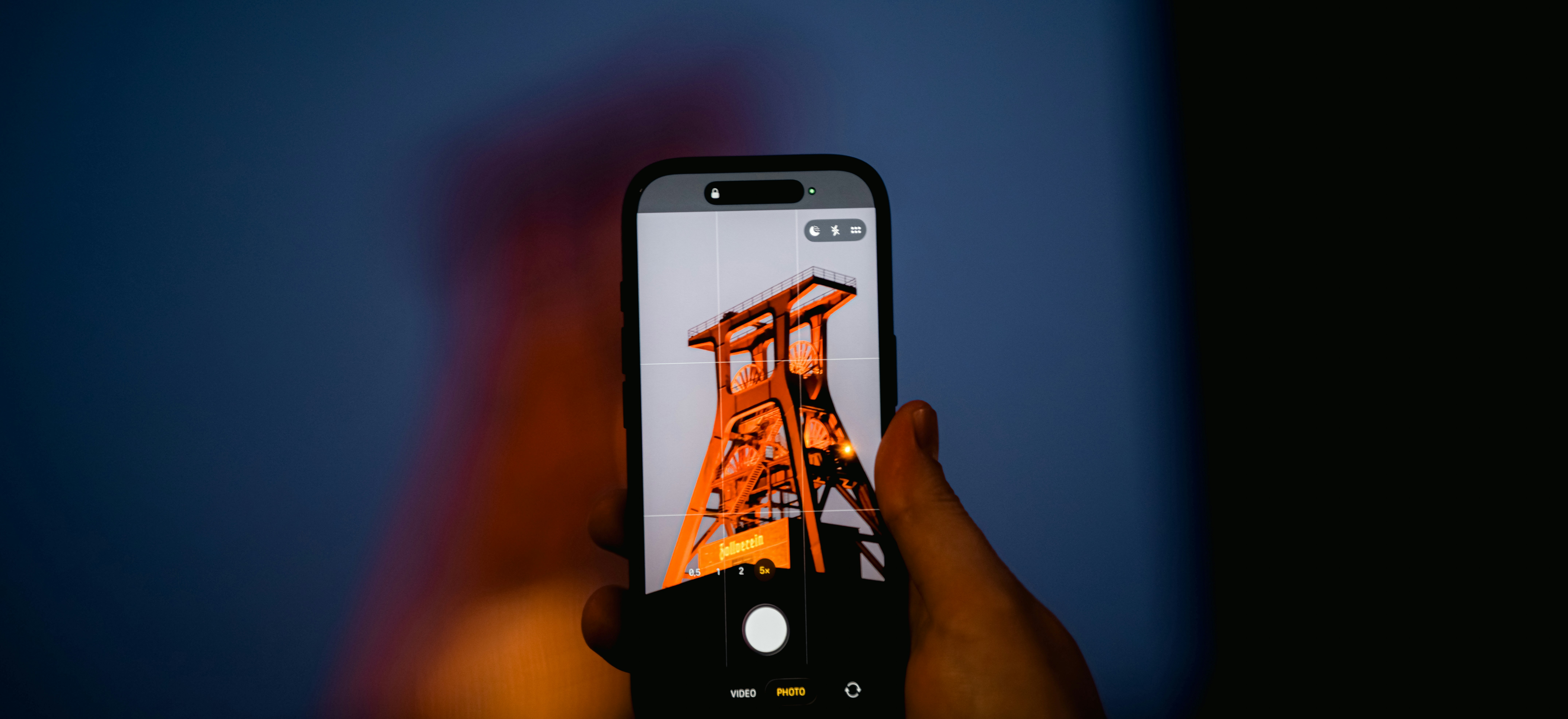 Smartphone capturing a tall industrial tower at night.