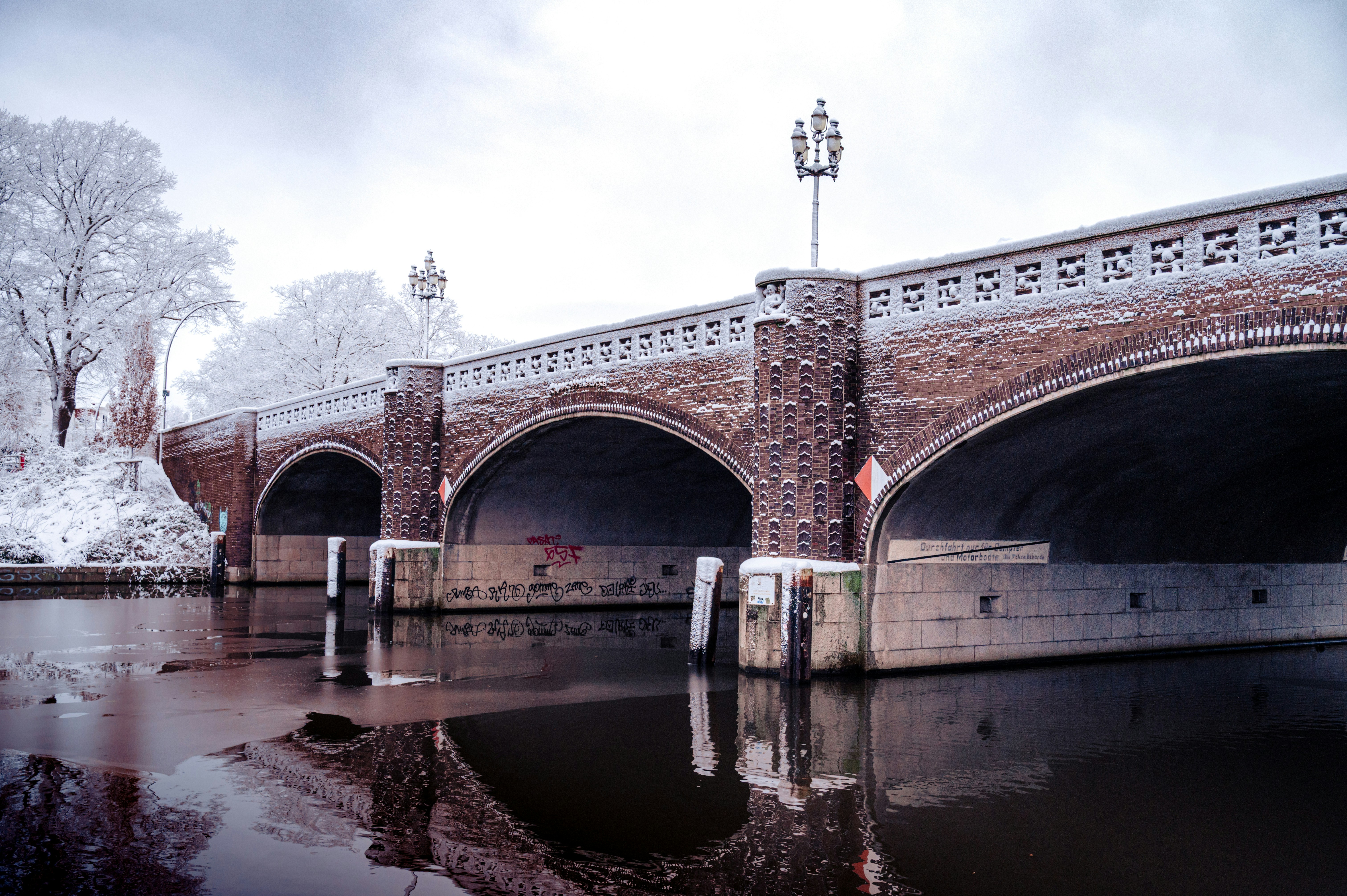A brick bridge arches over a calm river in winter.