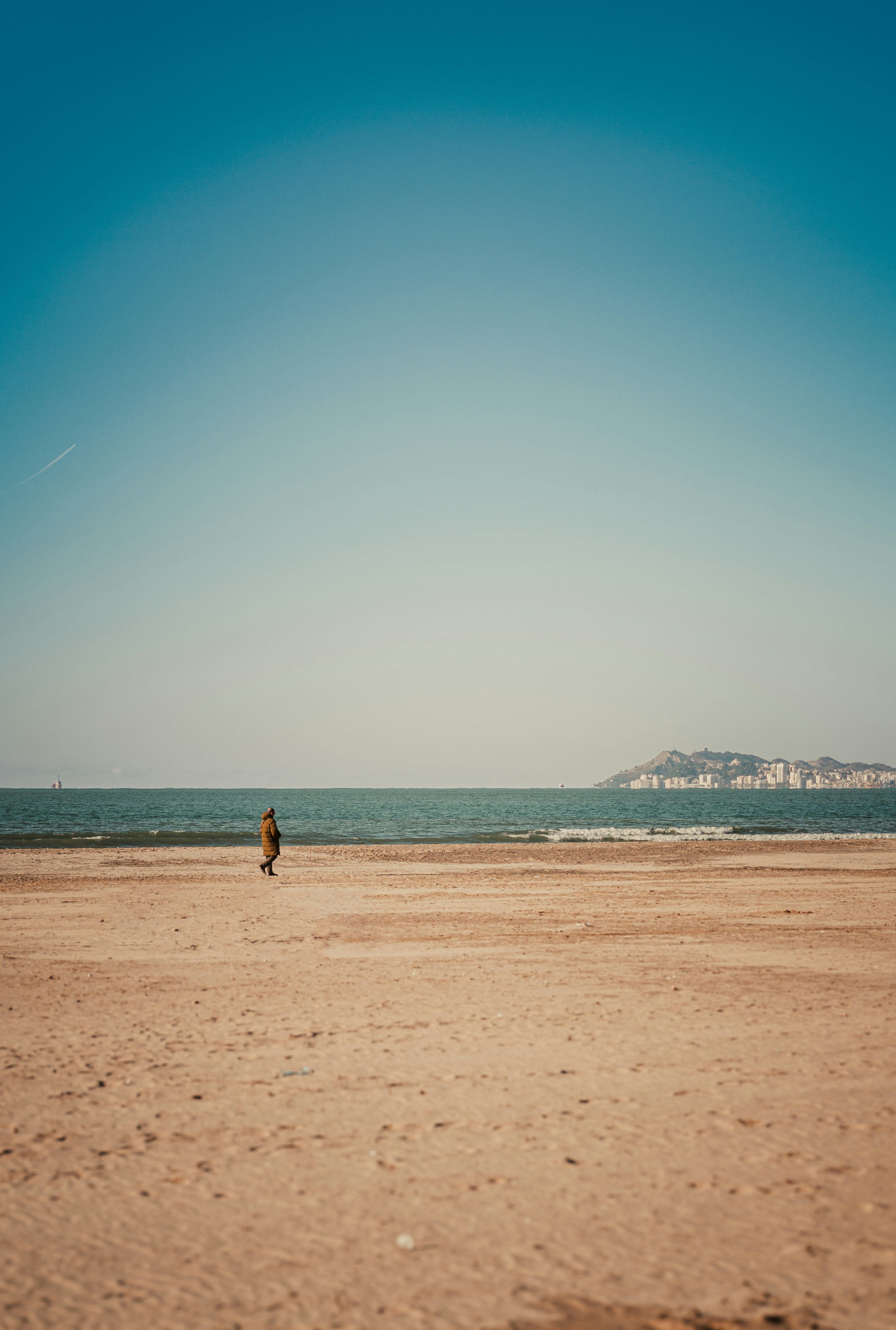 Lone figure walks on a sandy beach by the ocean.