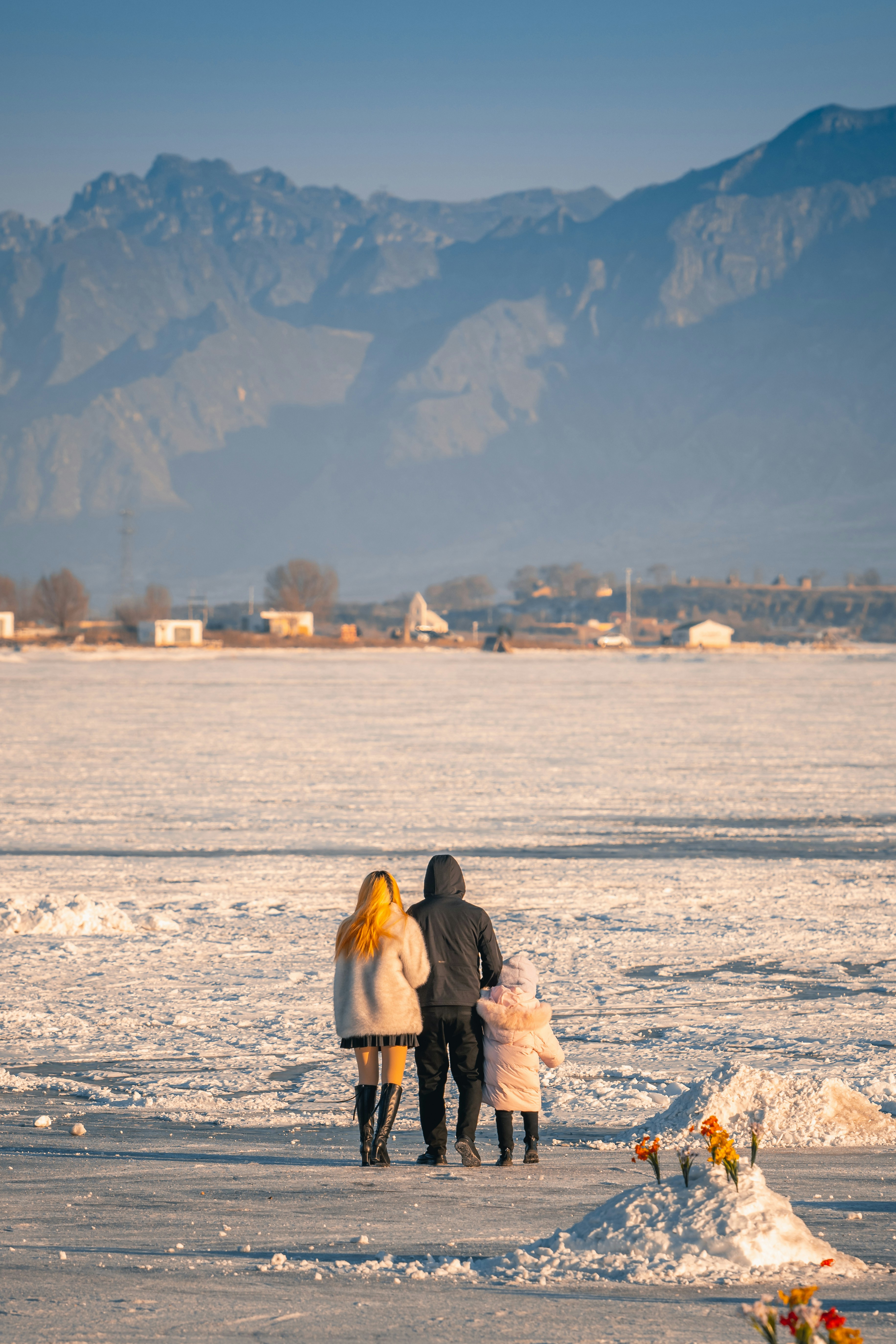Family standing on a frozen lake with mountains behind.