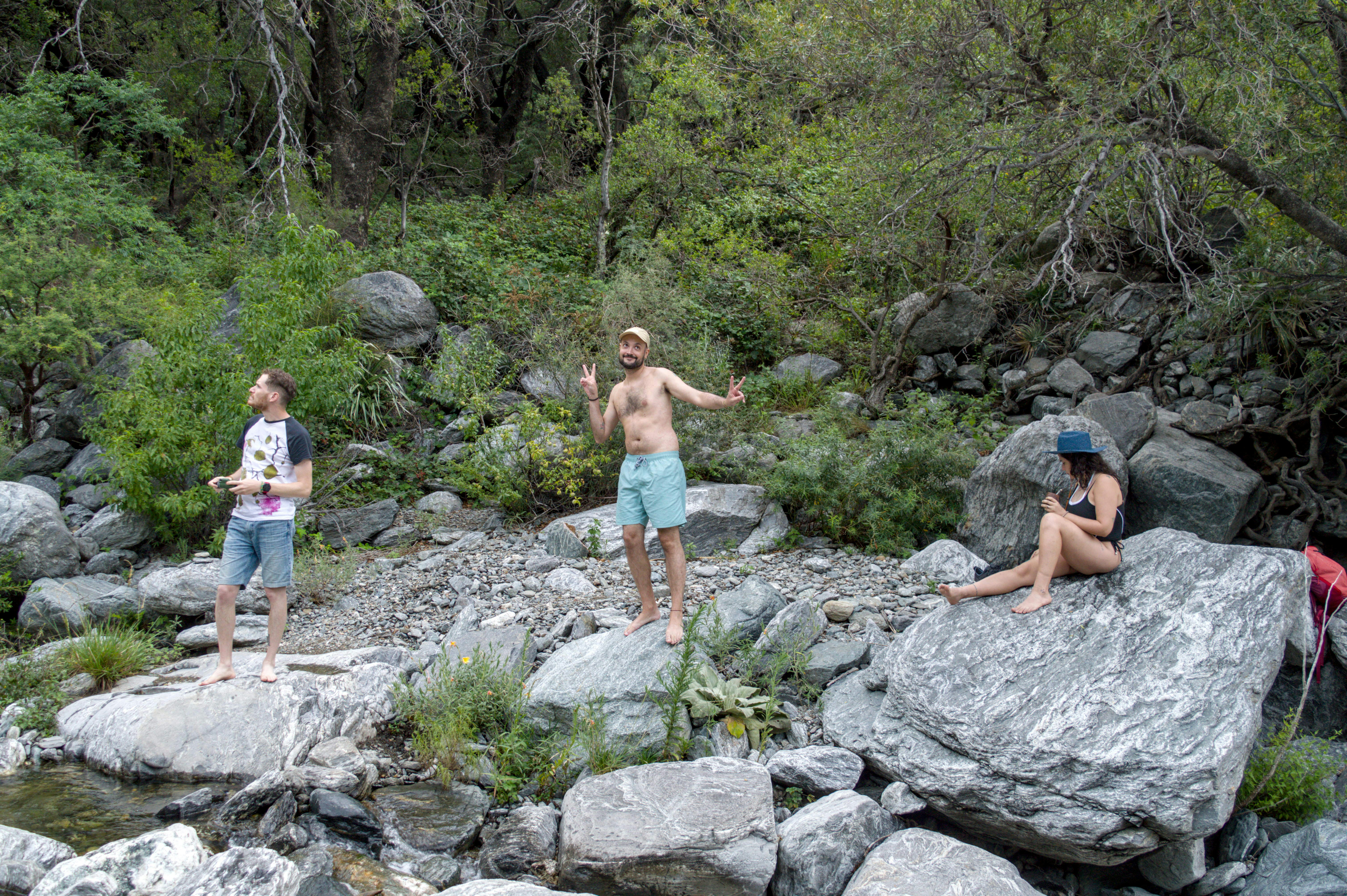 Three people relaxing by a rocky stream in nature.